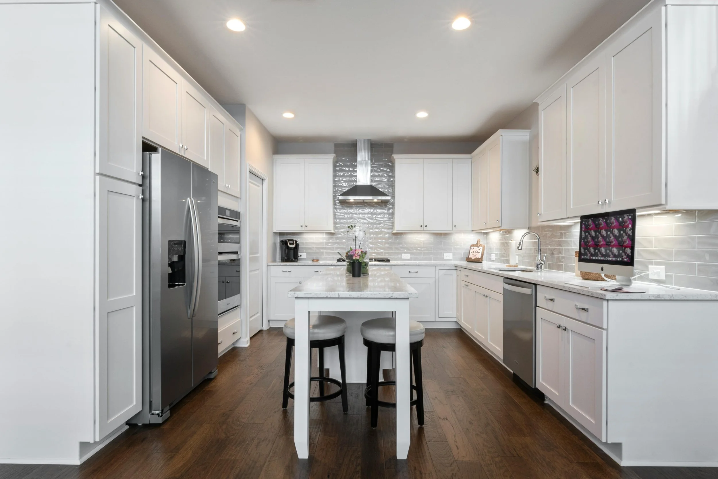 Modern kitchen with white cabinets, stainless steel appliances, marble island, and dark hardwood floors.