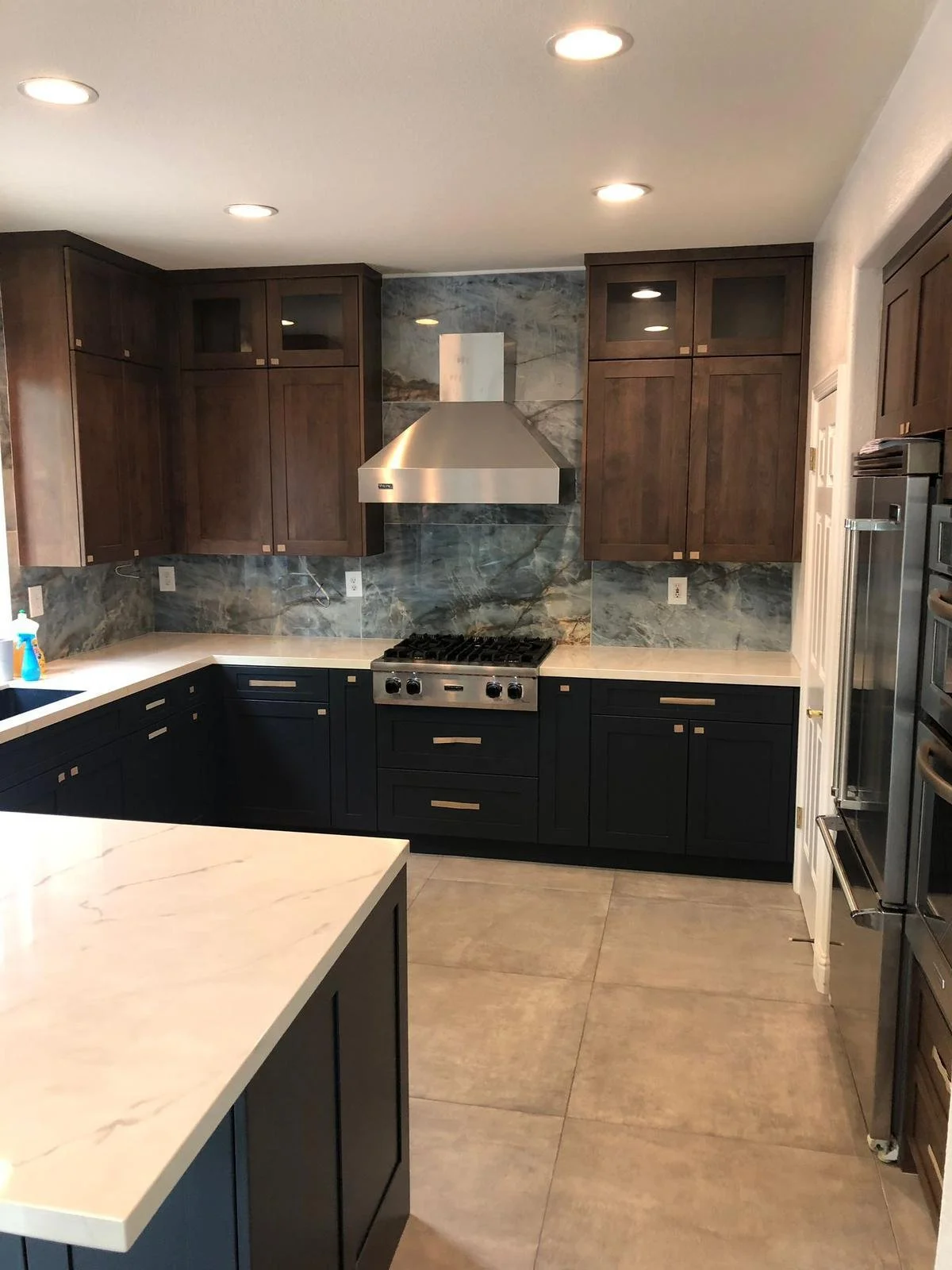 Modern kitchen with dark lower cabinets, wooden upper cabinets, marble backsplash, and stainless steel appliances including a stove and range hood.