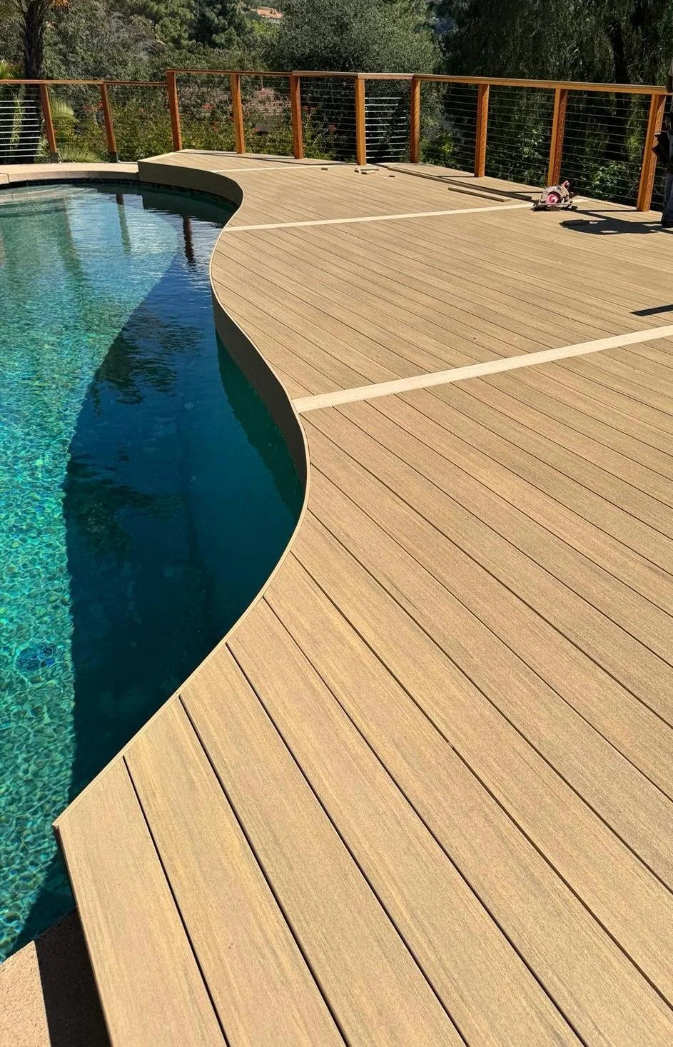 Empty wooden deck with a pool and a tribal-style wooden railing surrounding the area.