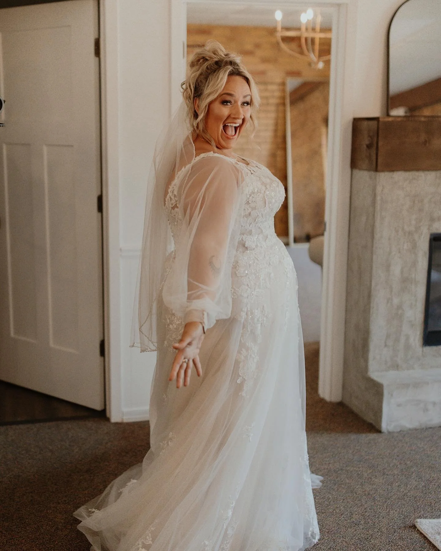 A woman in a wedding dress with a veil, smiling and playfully posing indoors.