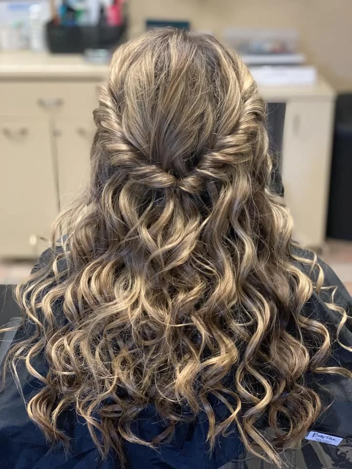 Back view of a woman with styled, curly, blonde hair featuring a half-up, twisted braid.