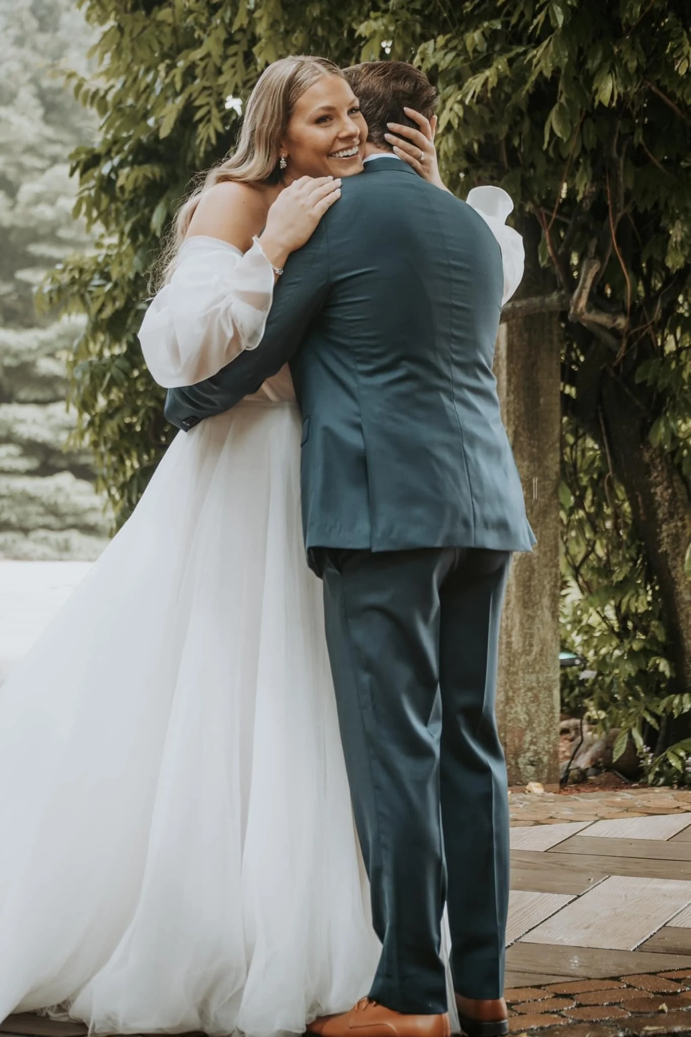 A bride and groom embrace outdoors during a wedding, with the bride smiling.