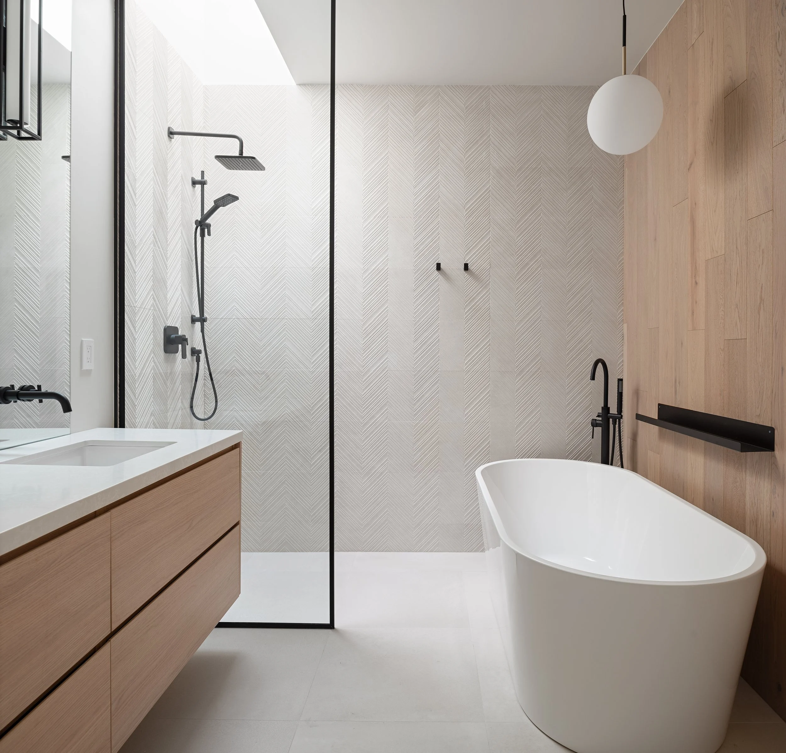 Modern bathroom with a white freestanding bathtub, black fixtures, wood accent wall, and a walk-in shower with black hardware, separated by a glass panel.