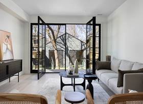 Living room with black-framed glass doors, white walls, gray sofa, black coffee table, and artwork on the wall, overlooking trees outside.
