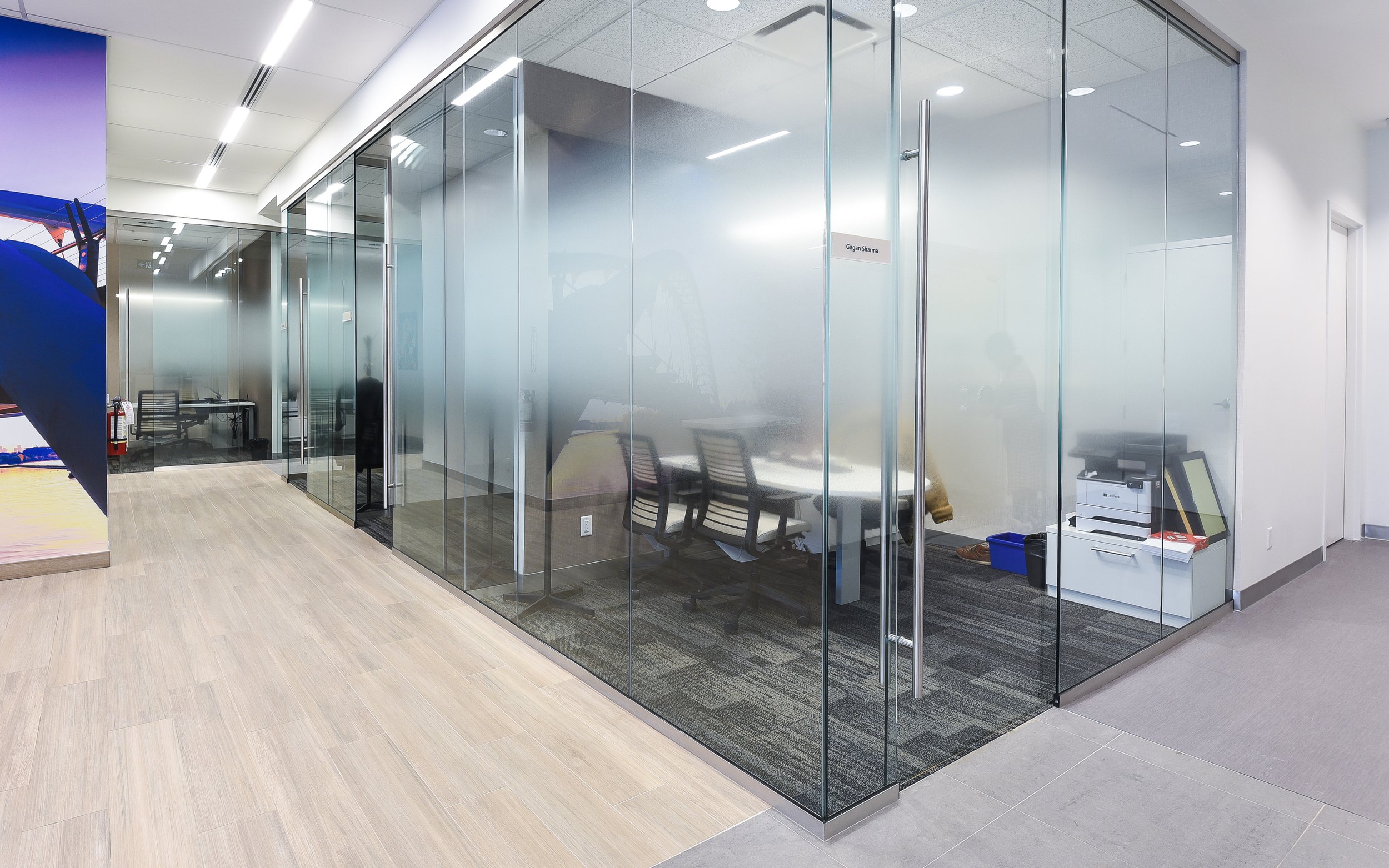 Glass-walled conference room with chairs, a table, and office equipment inside, in a modern office building.