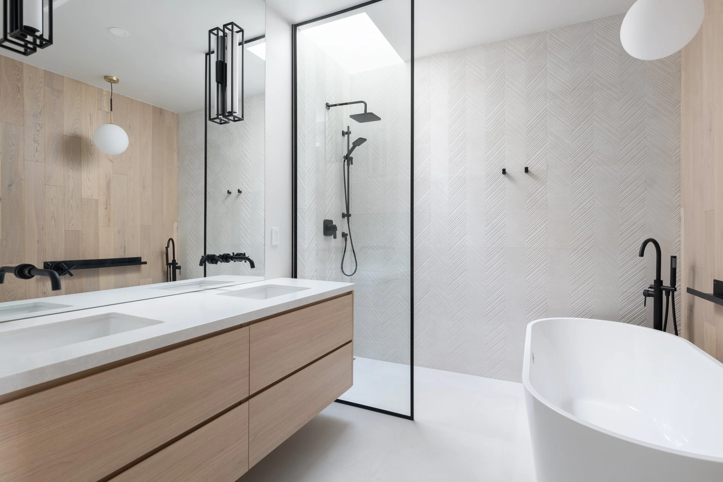Modern bathroom with double vanity, black fixtures, walk-in shower with black frame, and white freestanding bathtub.