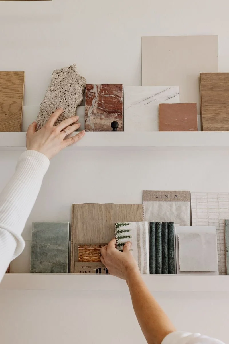 Hands of two people browsing through sample tiles and materials on display shelves.