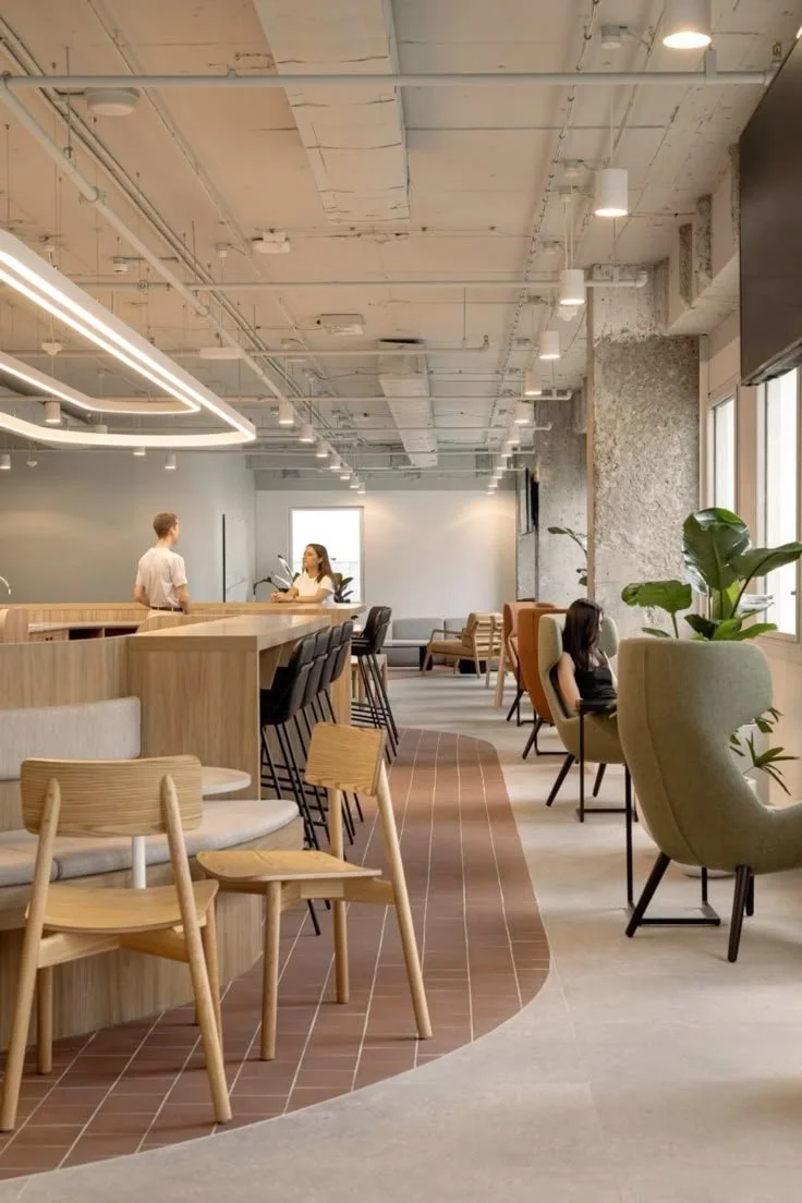 Modern indoor lounge with wooden chairs, a bar counter, and green plants, featuring large windows and minimalist decor.