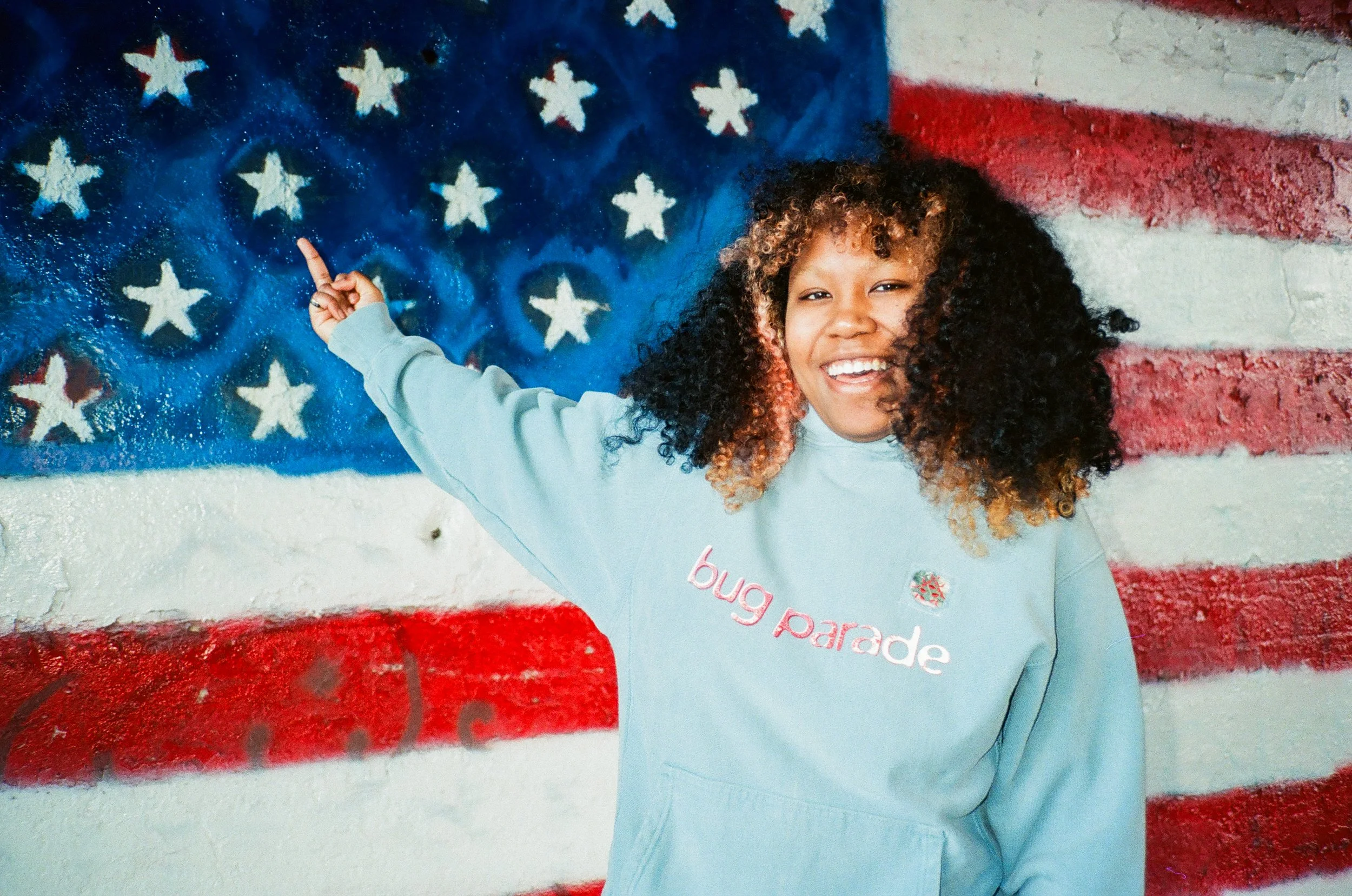 Girl smiling and pointing at a mural of a waving American flag with stars on a blue background.