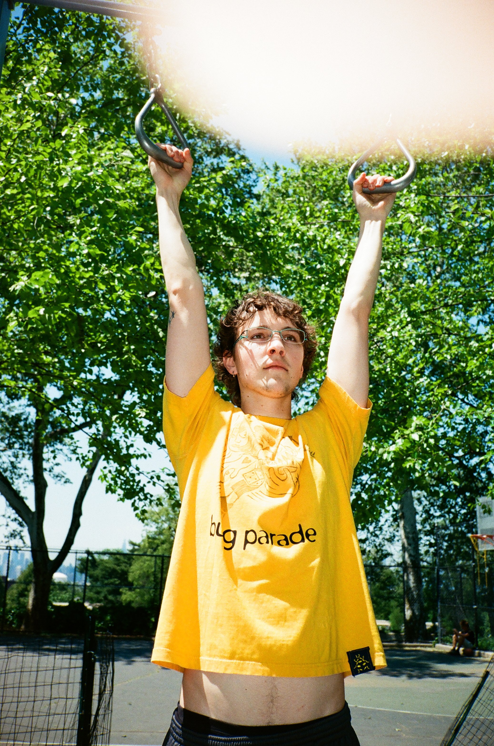 Person holding onto tennis court structure with trees and blue sky in the background.