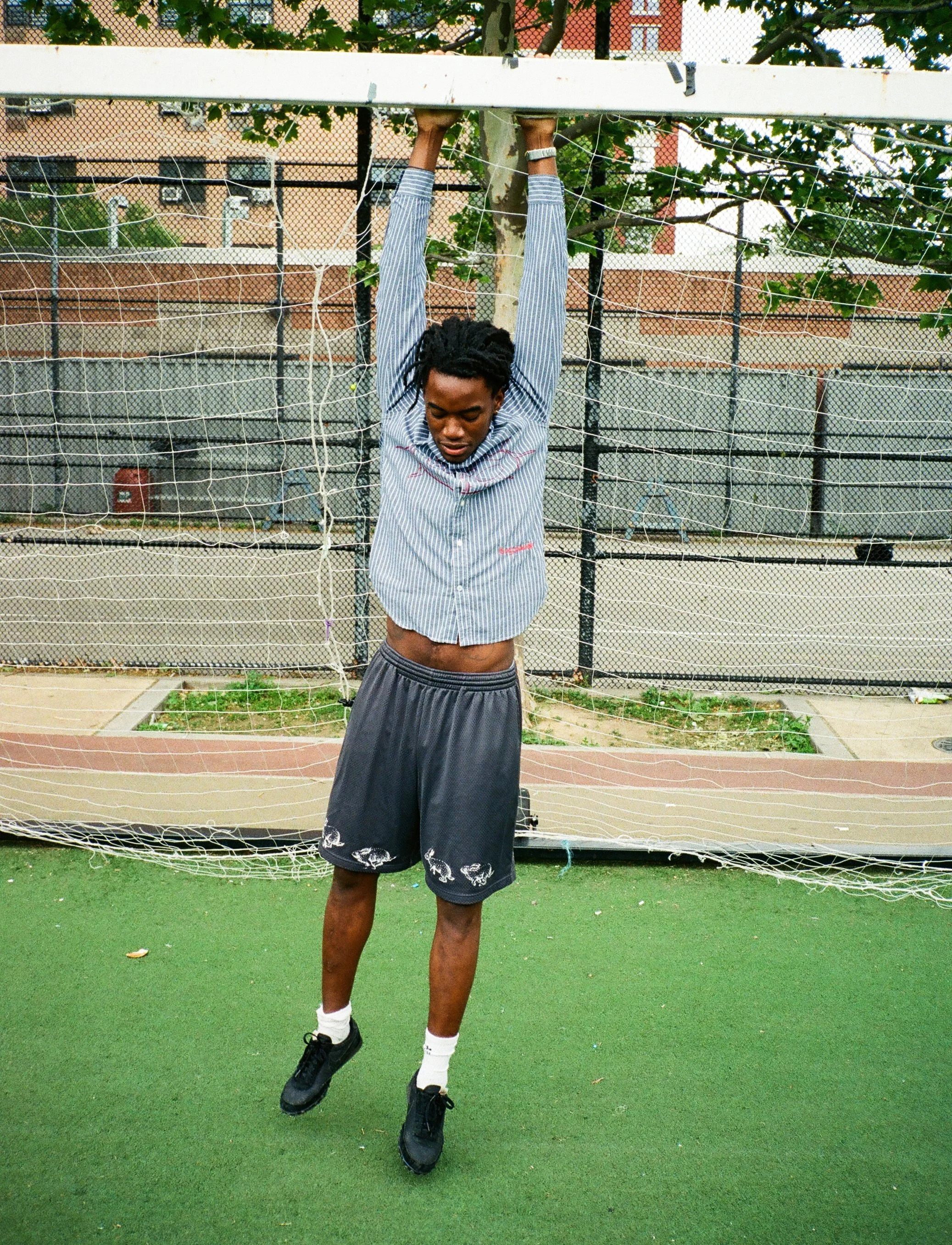 A young man hanging upside down from a soccer goal net on an outdoor sports court.