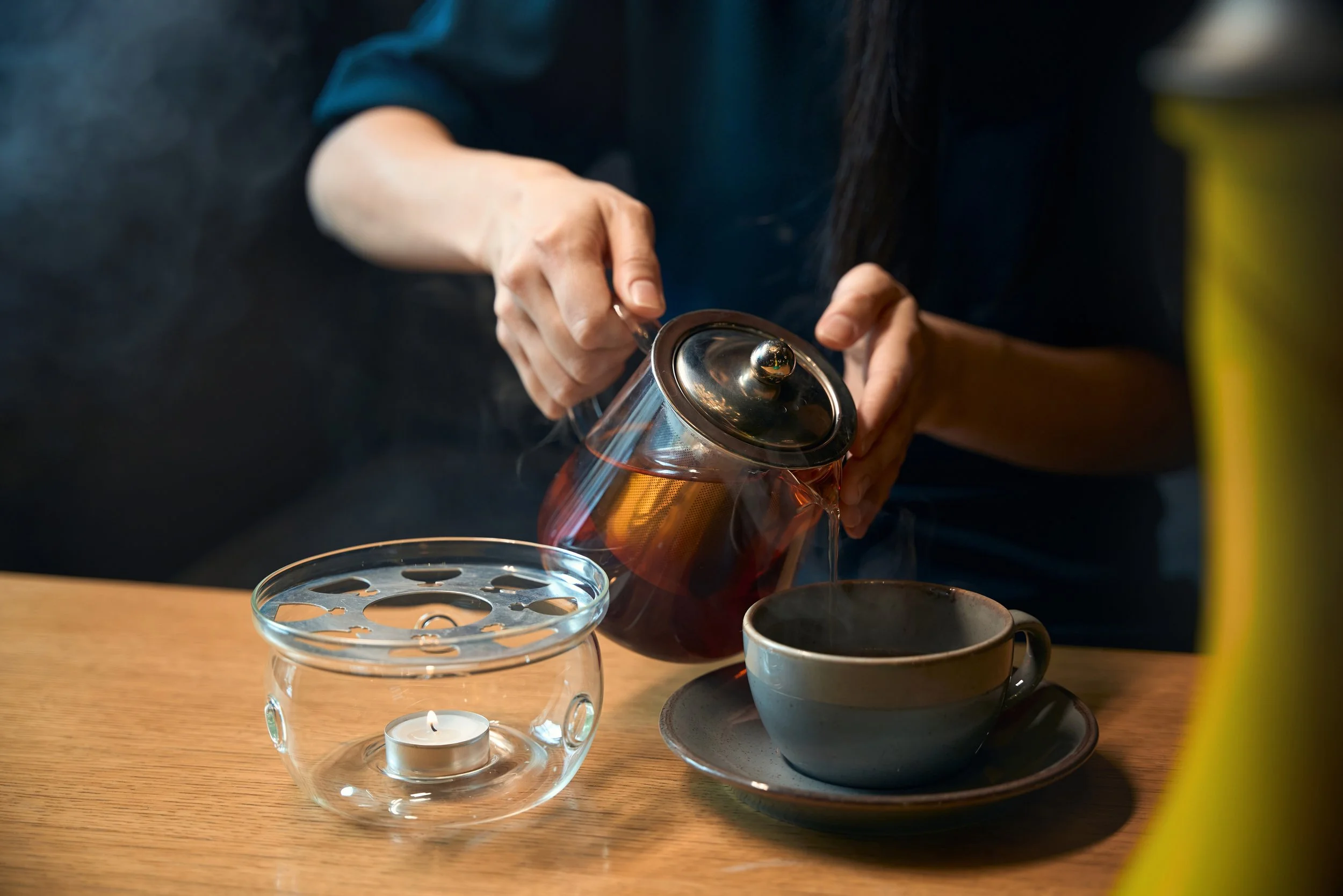 A soothing tea ritual as warm herbal tea is poured into a cup, candlelight adding a peaceful, mindful atmosphere of relaxation and self-care..jpg