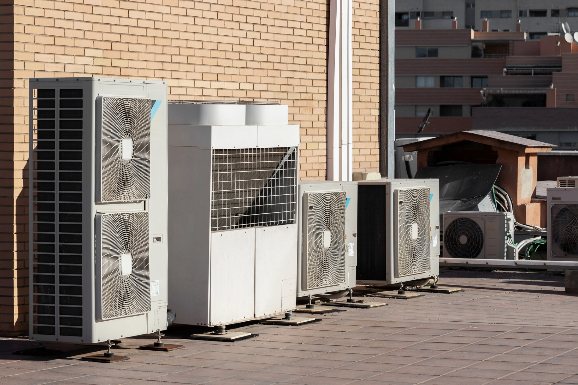 Unités de climatisation installées sur le toit d'un bâtiment, avec un mur en briques en arrière-plan.