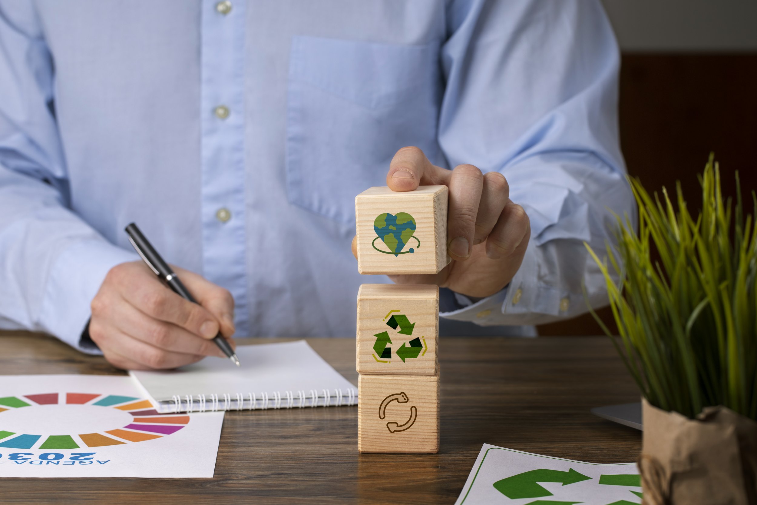 Un homme en chemise bleue dépose des blocs en bois illustrés avec des symboles de durabilité : un cœur avec la Terre, un symbole de recyclage, et un symbole de recyclage avec flèches tournantes.