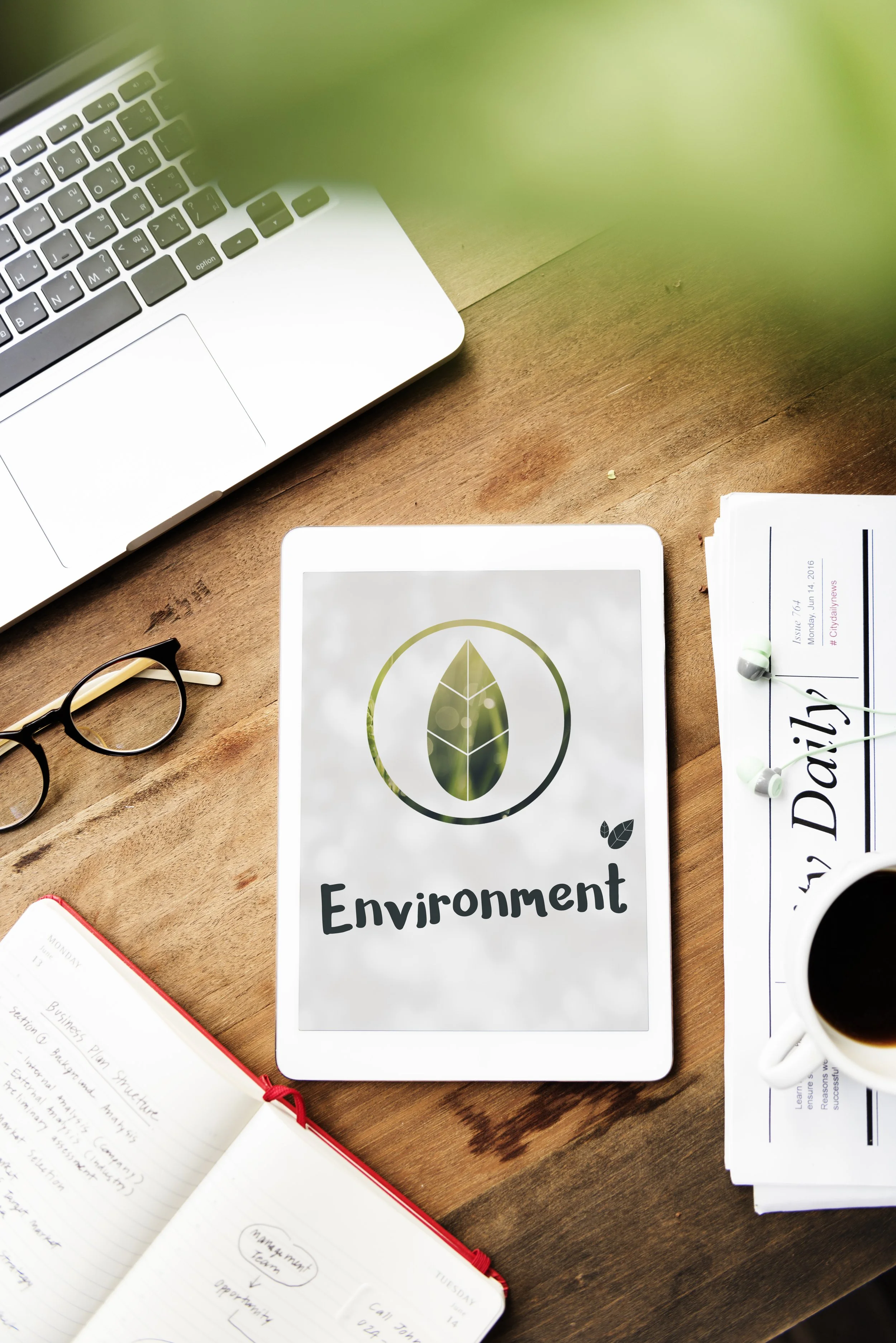 Une tablette avec le mot 'Environnement' et une feuille avec un logo de feuille sur un bureau en bois.