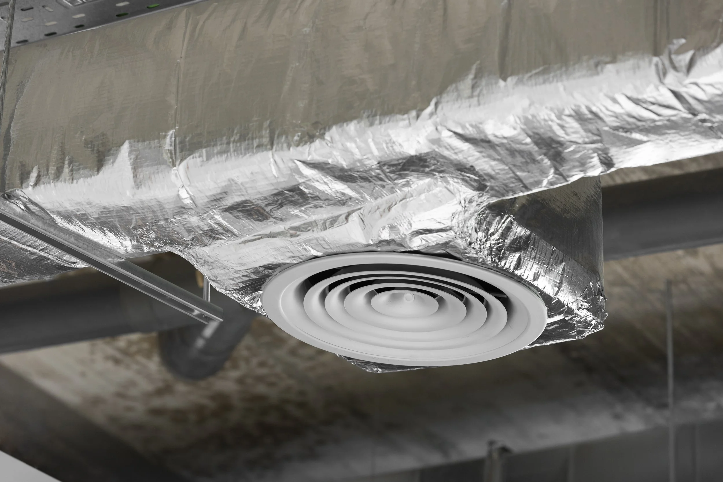 Diffuser de ventilation dans un plafond suspendu, entouré d'isolant en aluminium.