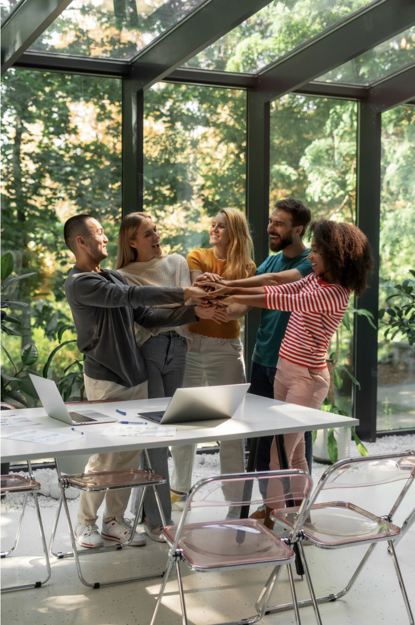 Cinq personnes en réunion dans une serre en verre, se tenant par les mains et souriant.