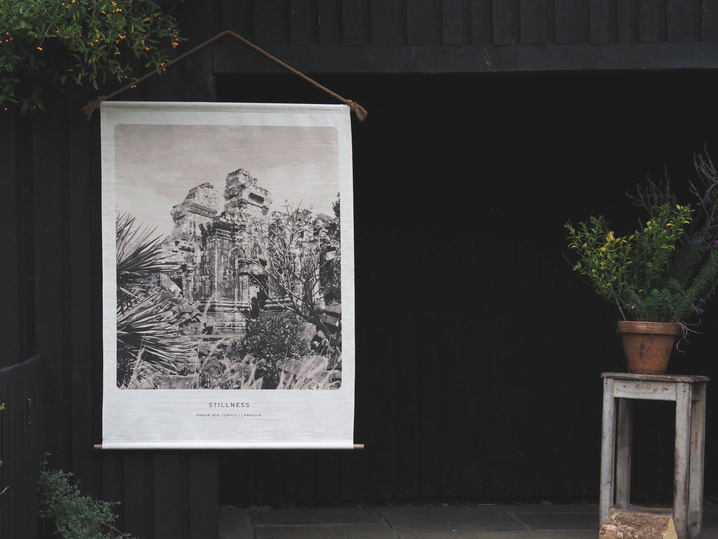Photograph of a black wood background, with focal point of a natural  organic linen wall hanging, featuring a black and white photographic image of an ancient temple of Phnom Bok in Angkor, Cambodia; photograph entitled Phnom Bok Sanctum Tower