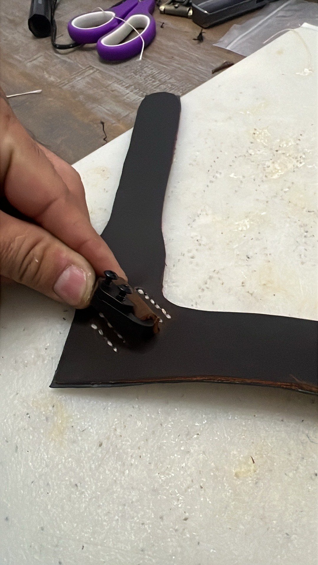 A person inspects the edge of a black surfboard with a wooden strip on a workbench.