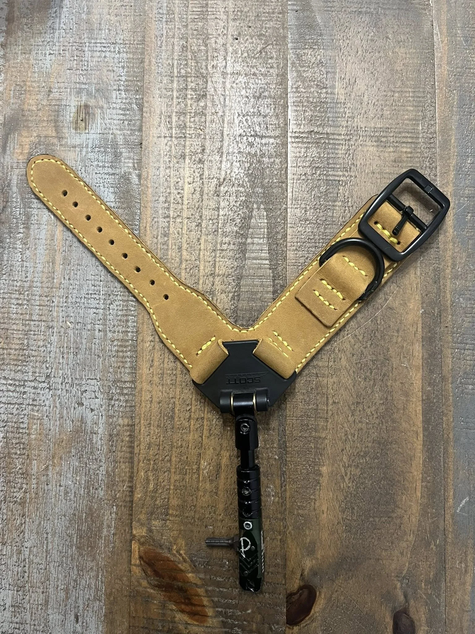 A yellow dog collar with black buckle and a metal tag, attached to a black metal clasp, on a wooden surface.
