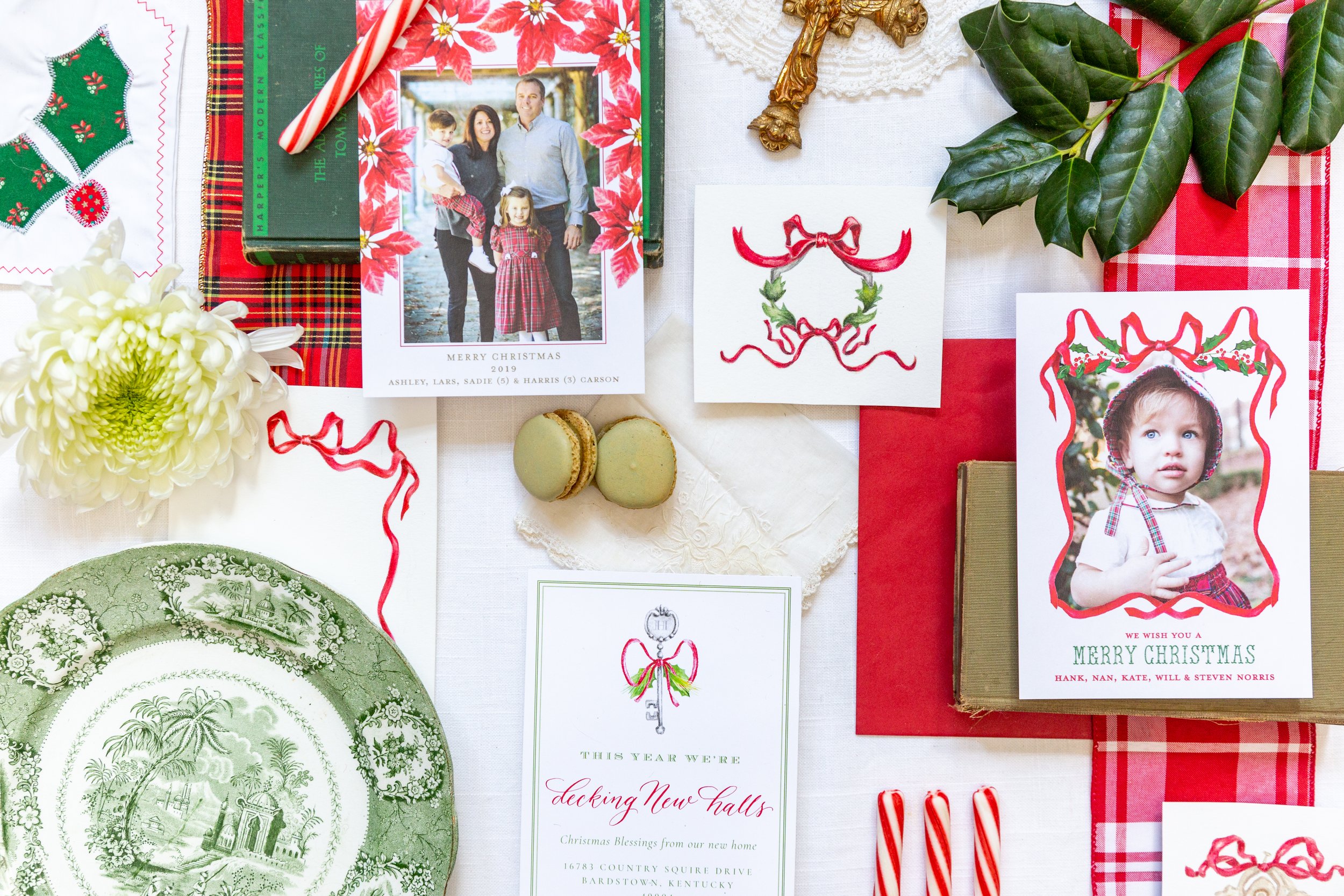 A flat lay of Christmas-themed items including holiday cards with family photos, decorative ornaments, green leaves, candy canes, cookies, and embroidered fabric with Christmas motifs.