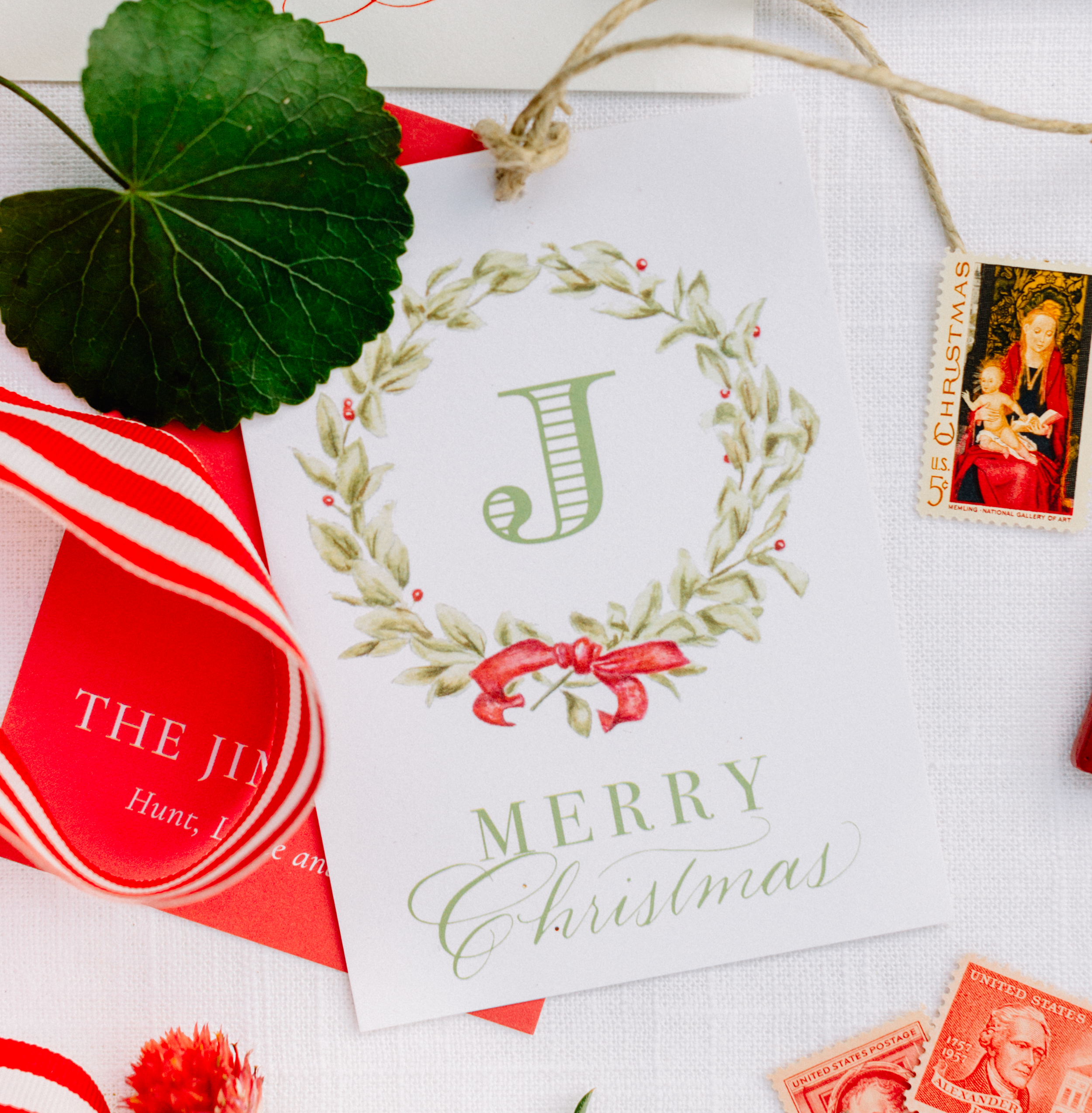 Close-up of Christmas cards, postage stamps, and a flower on a white surface, with red ribbon.