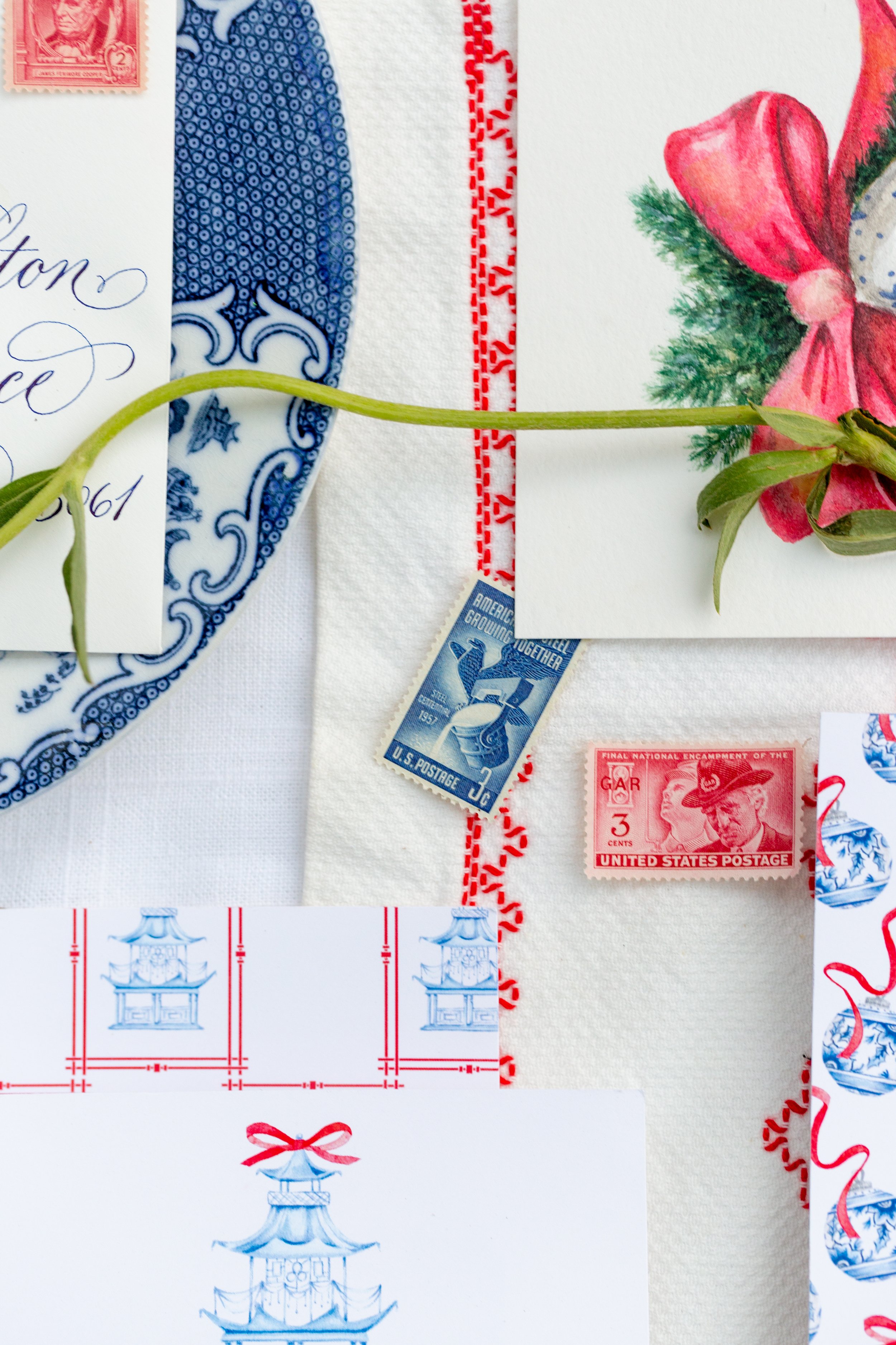 Close-up of vintage American postage stamps including a red 3-cent stamp, a blue 1-cent stamp, and a red 2-cent stamp, with decorative paper and ribbon patterns in the background.