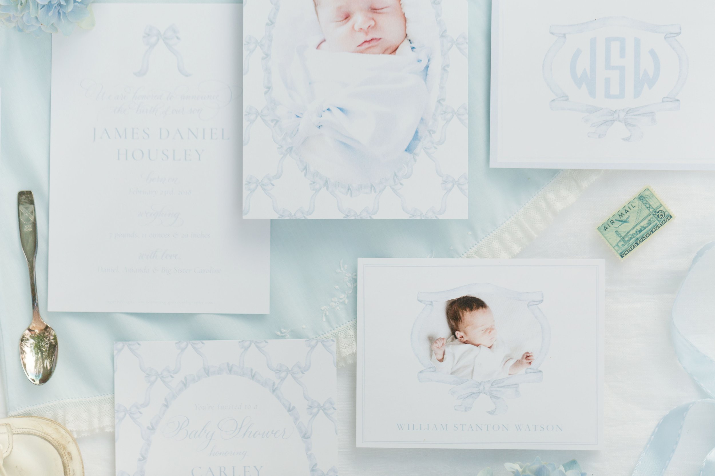 A baby asleep on a white cloth, surrounded by baby shower invitations and decorative elements on a table.