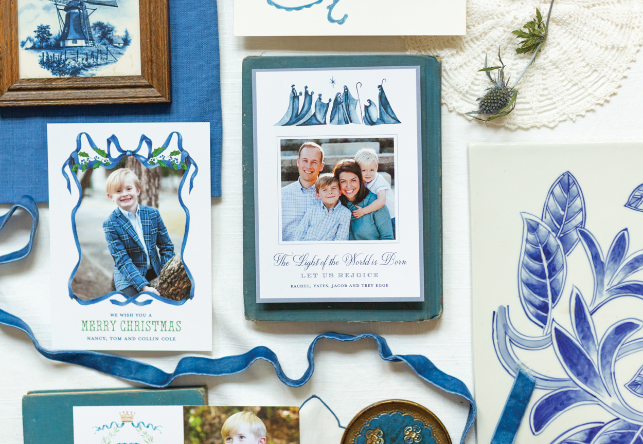 Collection of family and holiday greeting cards with photographs, illustrations of nativity wise men and decorative leaves, arranged among dried berries and painted pottery.