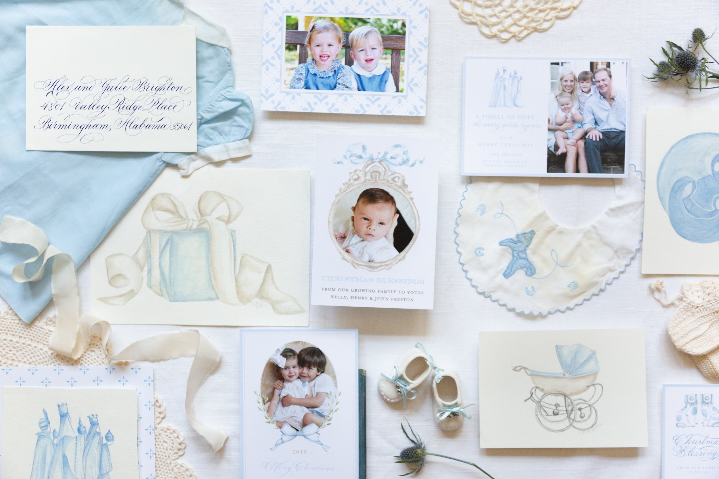 A collection of holiday photos, greeting cards, and decorative items on a white surface, including pictures of children and a family, Christmas-themed artwork, and handwritten addresses.