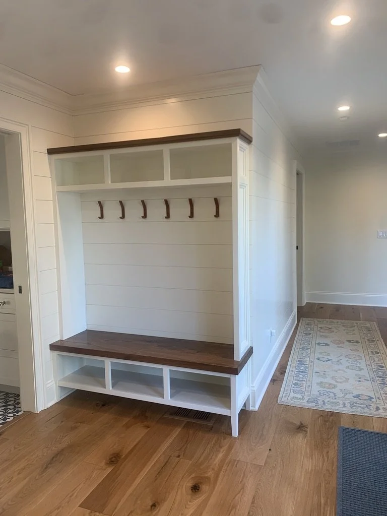 Entryway mudroom with built-in bench, hooks, and shelves, featuring white and stained wood finishes in a modern home.