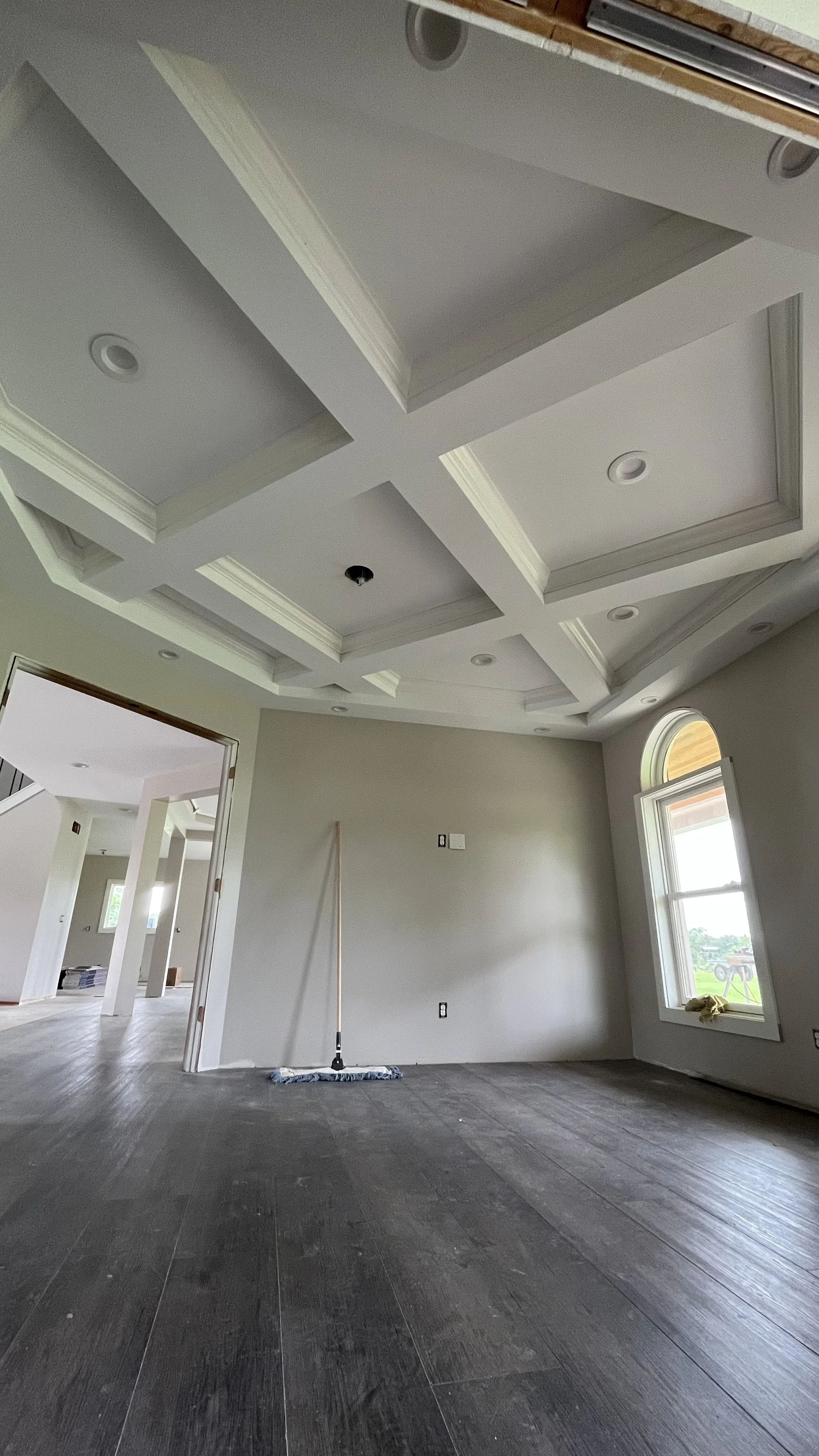 Empty room with dark wood floors, newly painted walls, ceiling with decorative molding, large window, and construction tools.