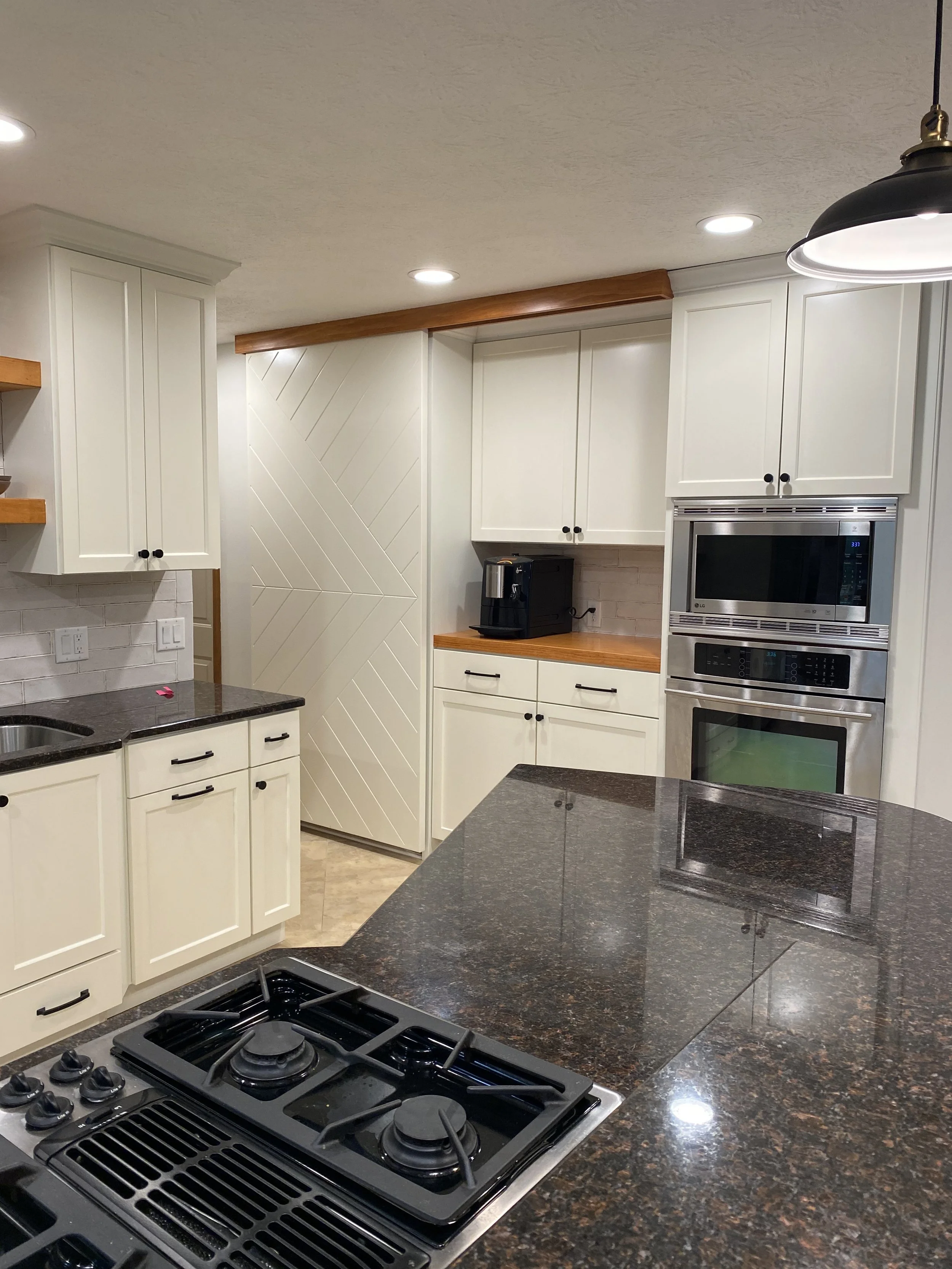 Kitchen with white cabinets, black granite countertops, stainless steel appliances including a microwave and oven, a black coffee maker, and a gas cooktop. Recessed lighting and a black pendant light are visible.
