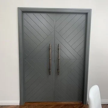 Dark gray double doors with vertical handles, set in a light-colored wall.