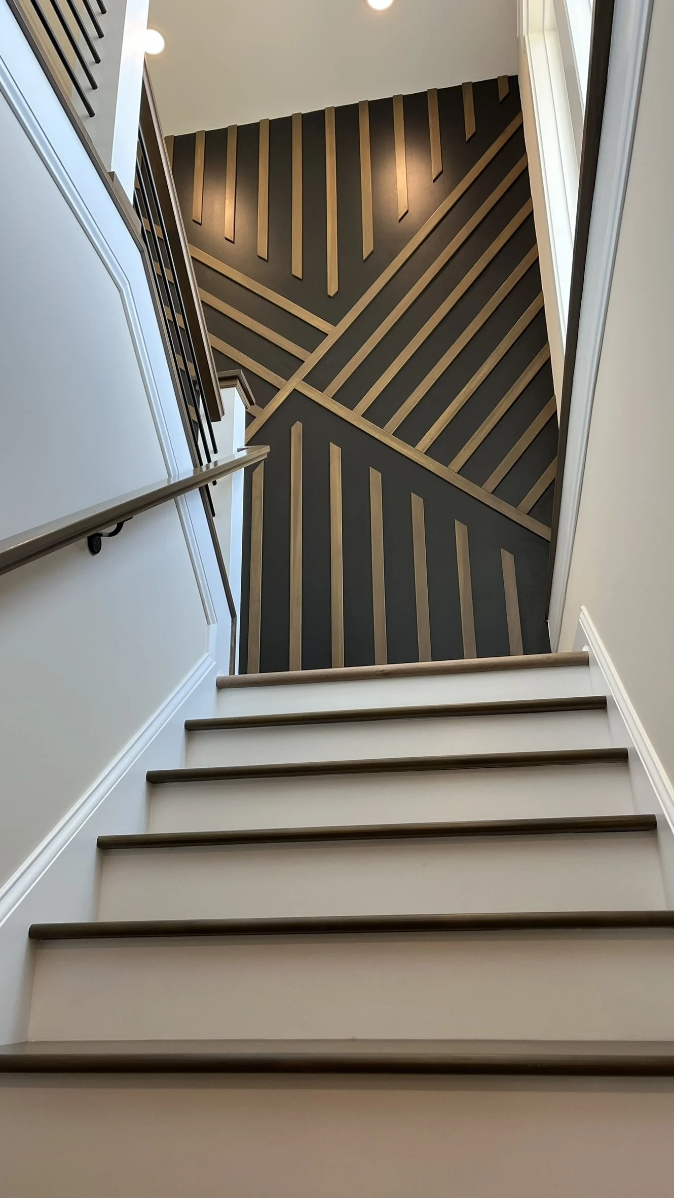 View from the bottom of staircase looking up at the hardwood and carpeted stairs, with a geometric patterned wall on the landing.