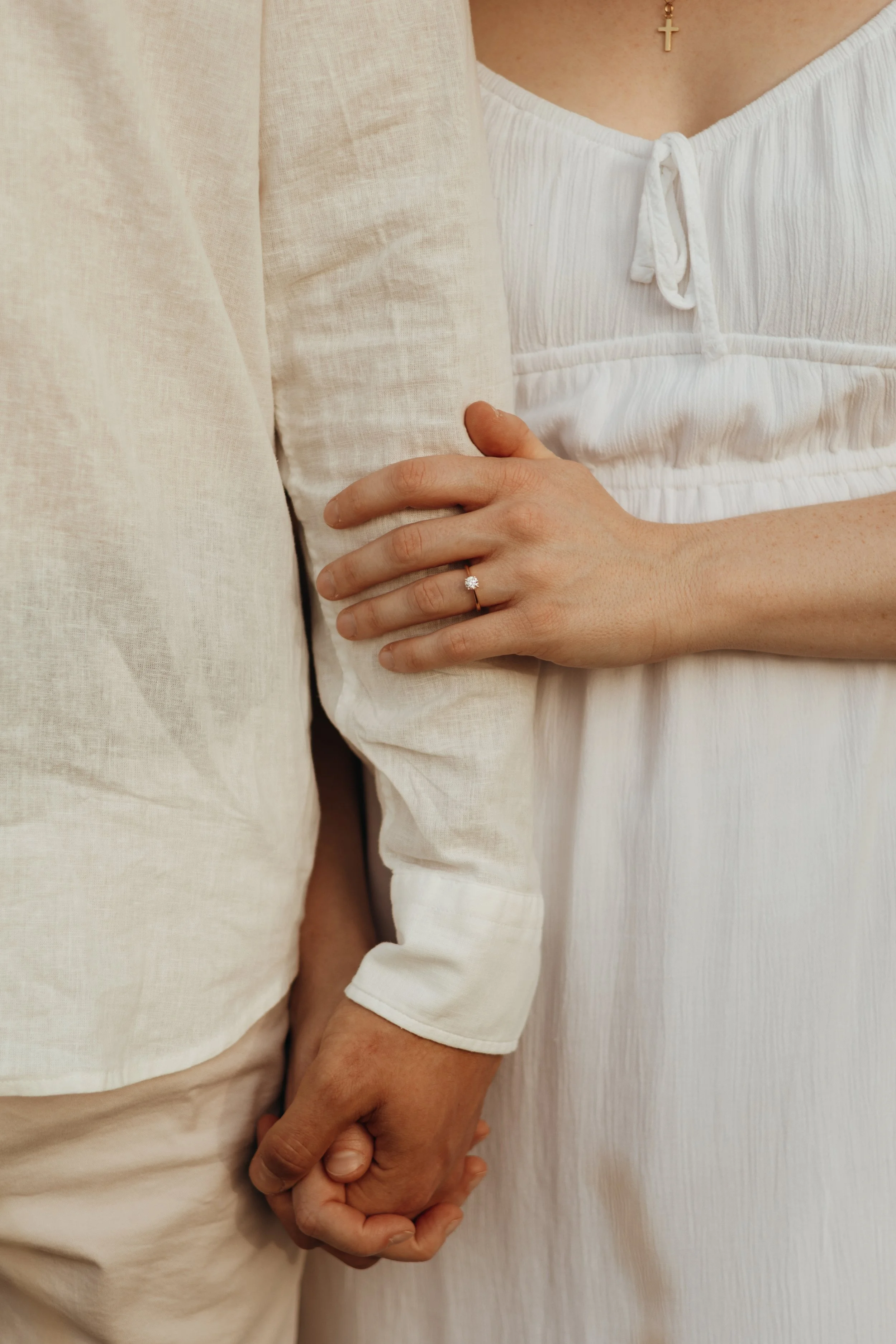 Nahaufnahme eines Paares, das sich an den Händen hält. Die Frau trägt einen Verlobungsring mit Diamant auf ihrem Ringfinger.