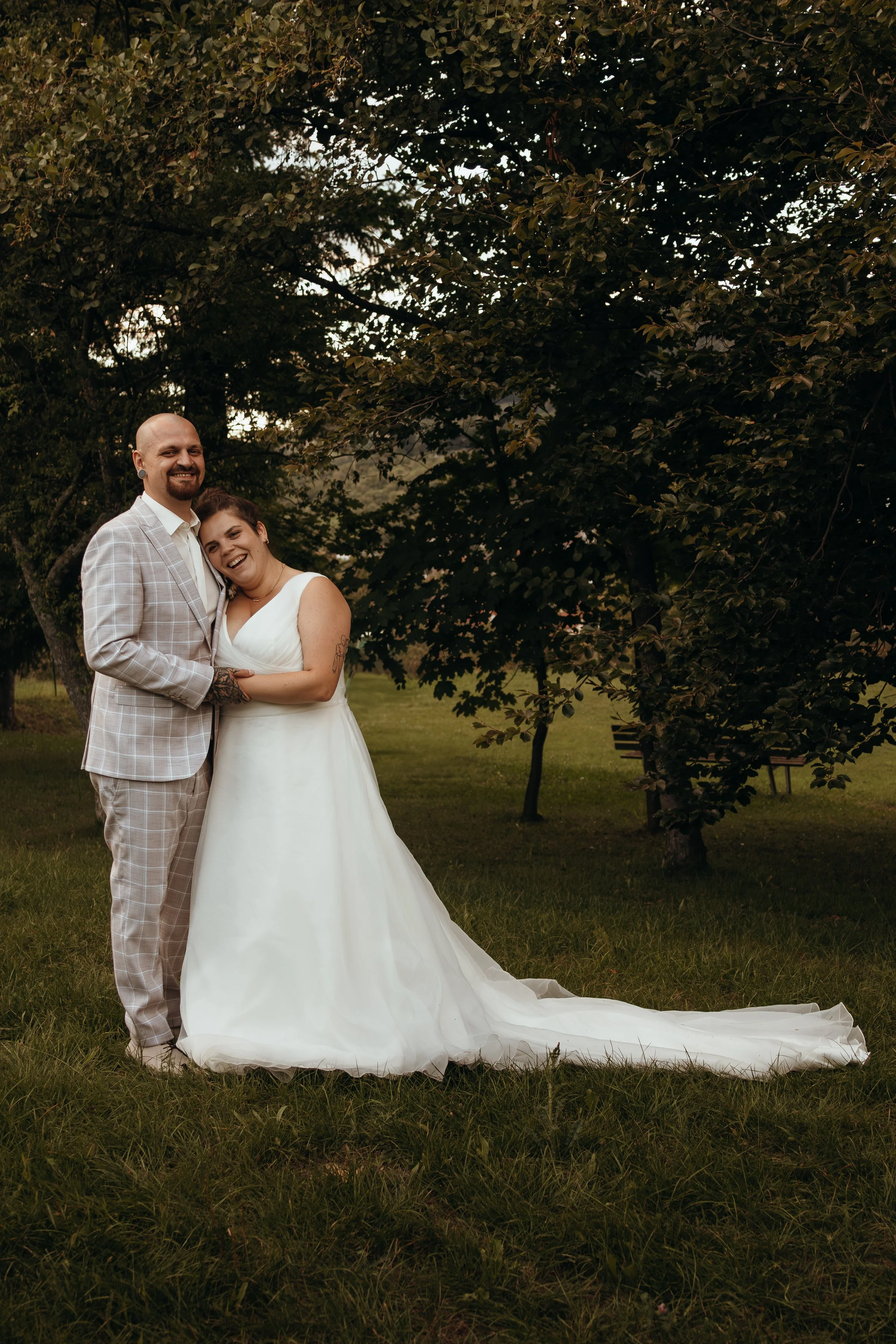 Ein glückliches Paar bei einer Hochzeit im Freien, umgeben von Bäumen und Gras.