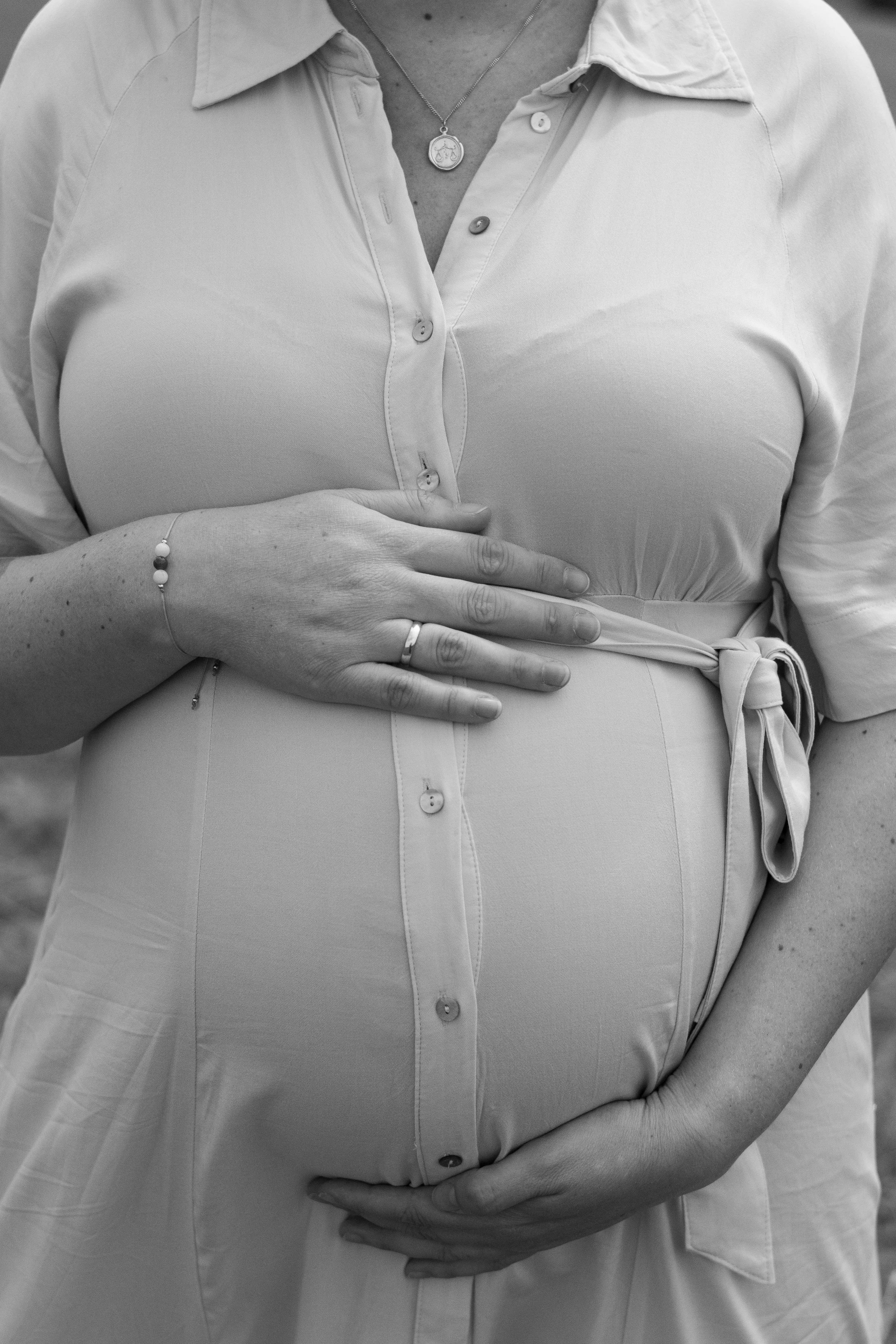 Schwangere Frau in gemessenem Licht mit Hand auf dem Bauch, getragen in einem Hemd, schwarz-weiß Fotografie.