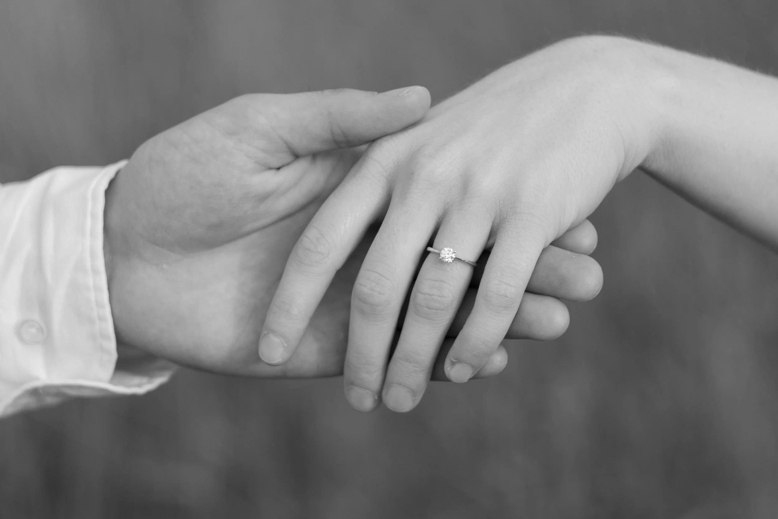 Nahaufnahme von zwei Händen, eine mit einem Verlobungsring, die andere legt die Hand darauf, schwarz-weiß