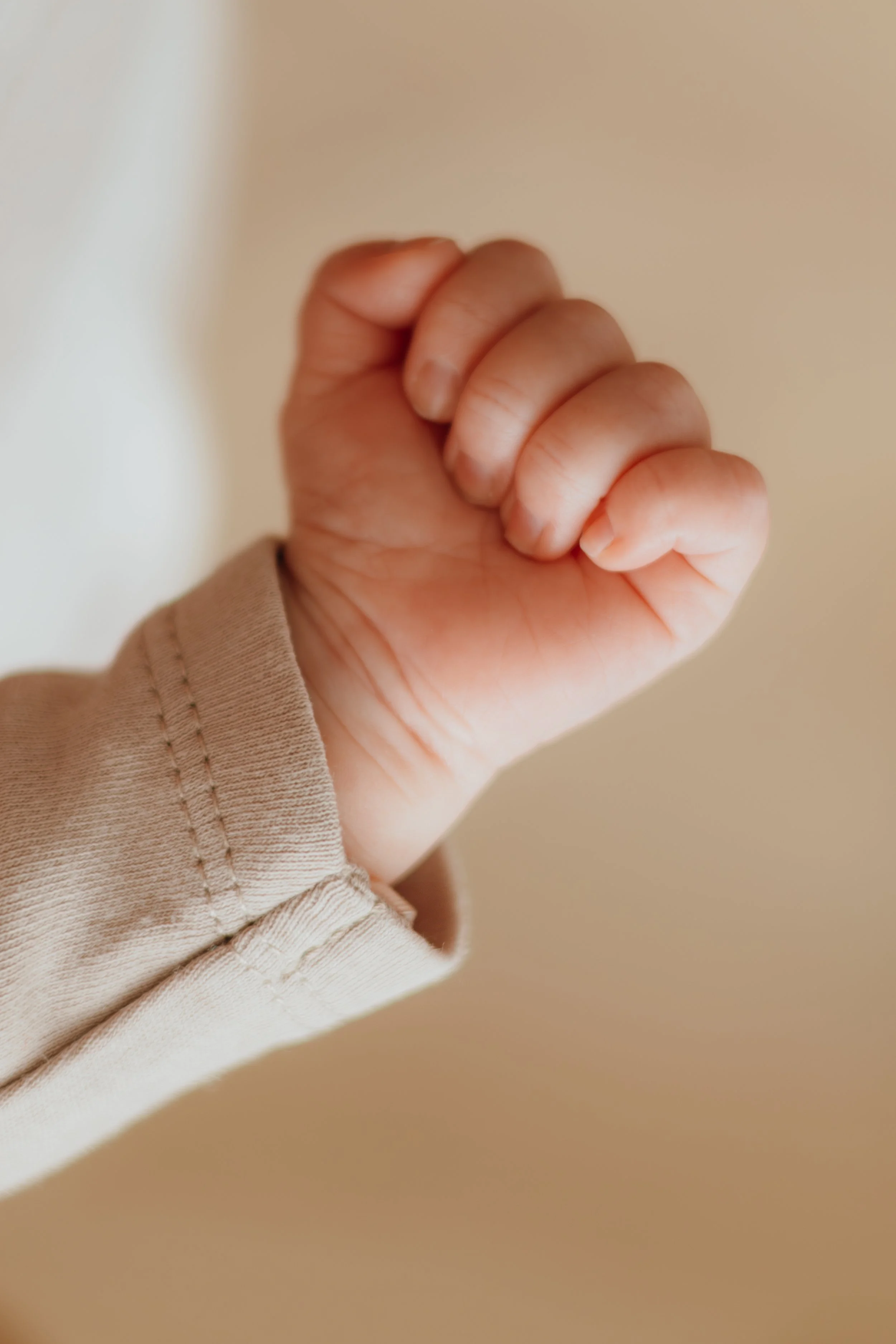 Nahaufnahme einer kleinen Kinderfaust, die die Hand einer Person ist, in einem beige Hemd oder Pullover geklammert.