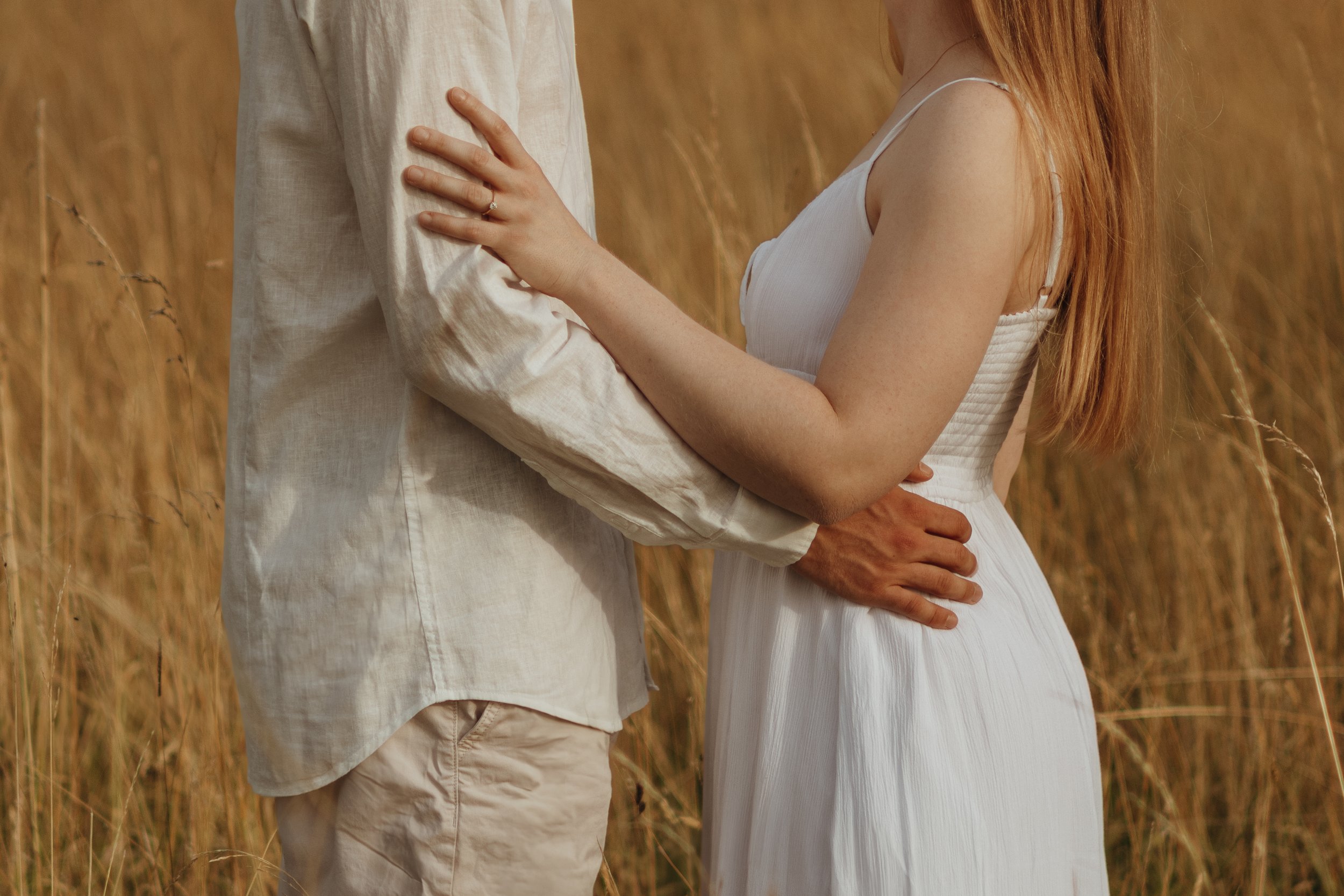 Nahaufnahme eines Paares, das sich in einem Feld umarmt, mit Fokus auf ihre Arme und Körper, beide tragen weiße Kleidung.