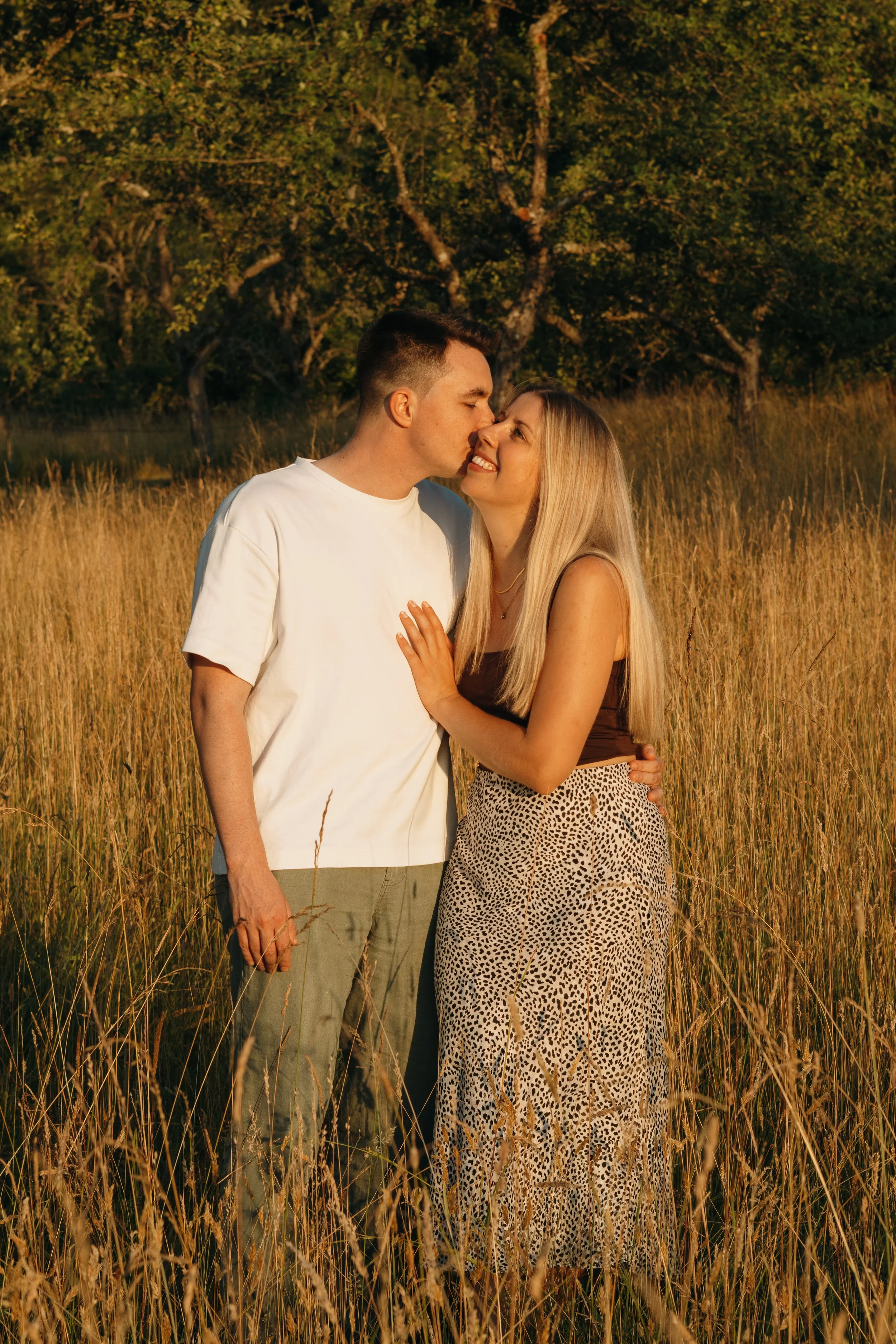 Ein Liebespaar, das in einem Feld im Sonnenuntergang steht und einander küsst.