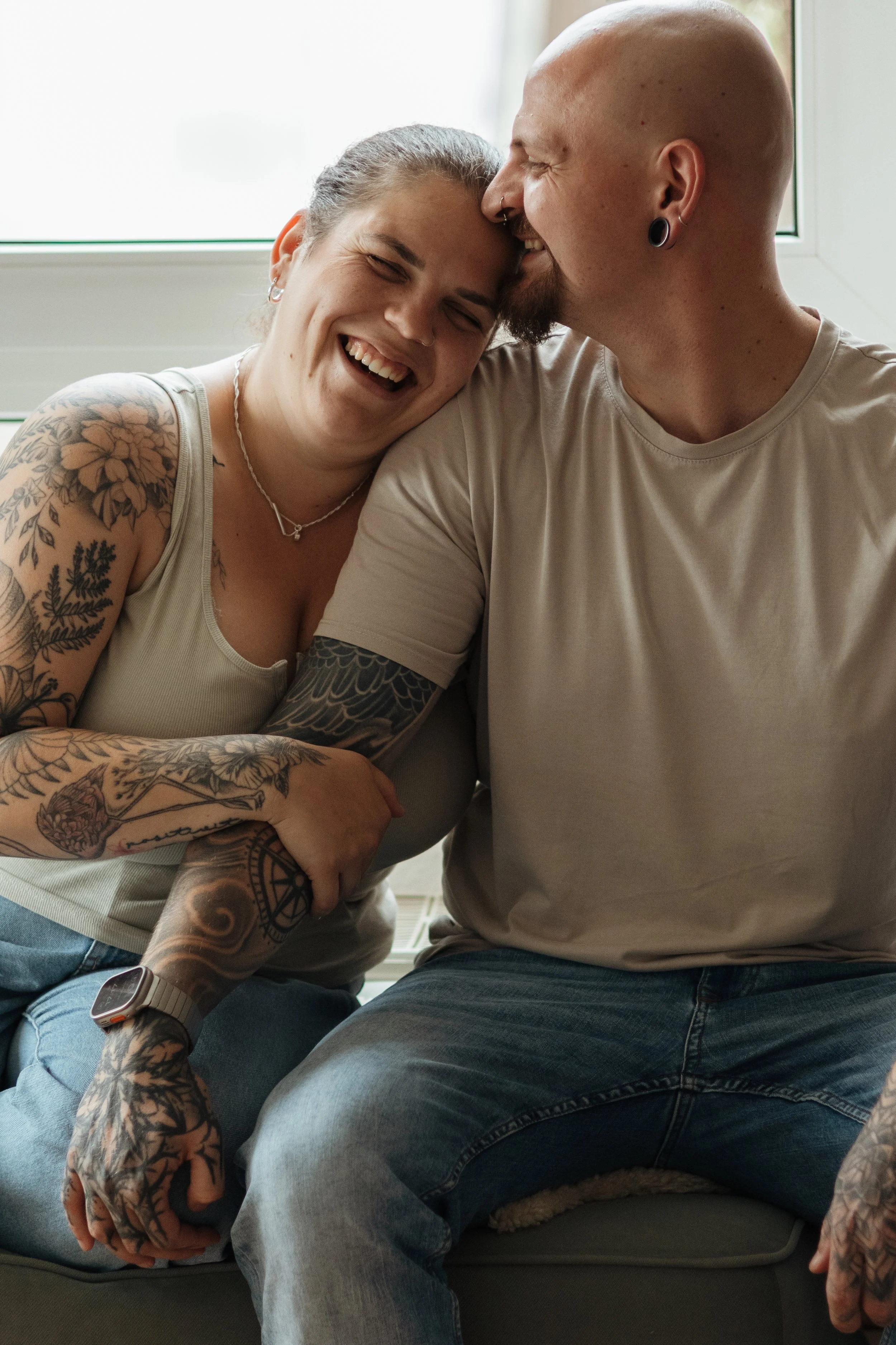 Ein lachendes Paar sitzt auf einer Couch, in einem hell erleuchteten Raum, das Paar ist sehr glücklich und zeigt Zuneigung zueinander.