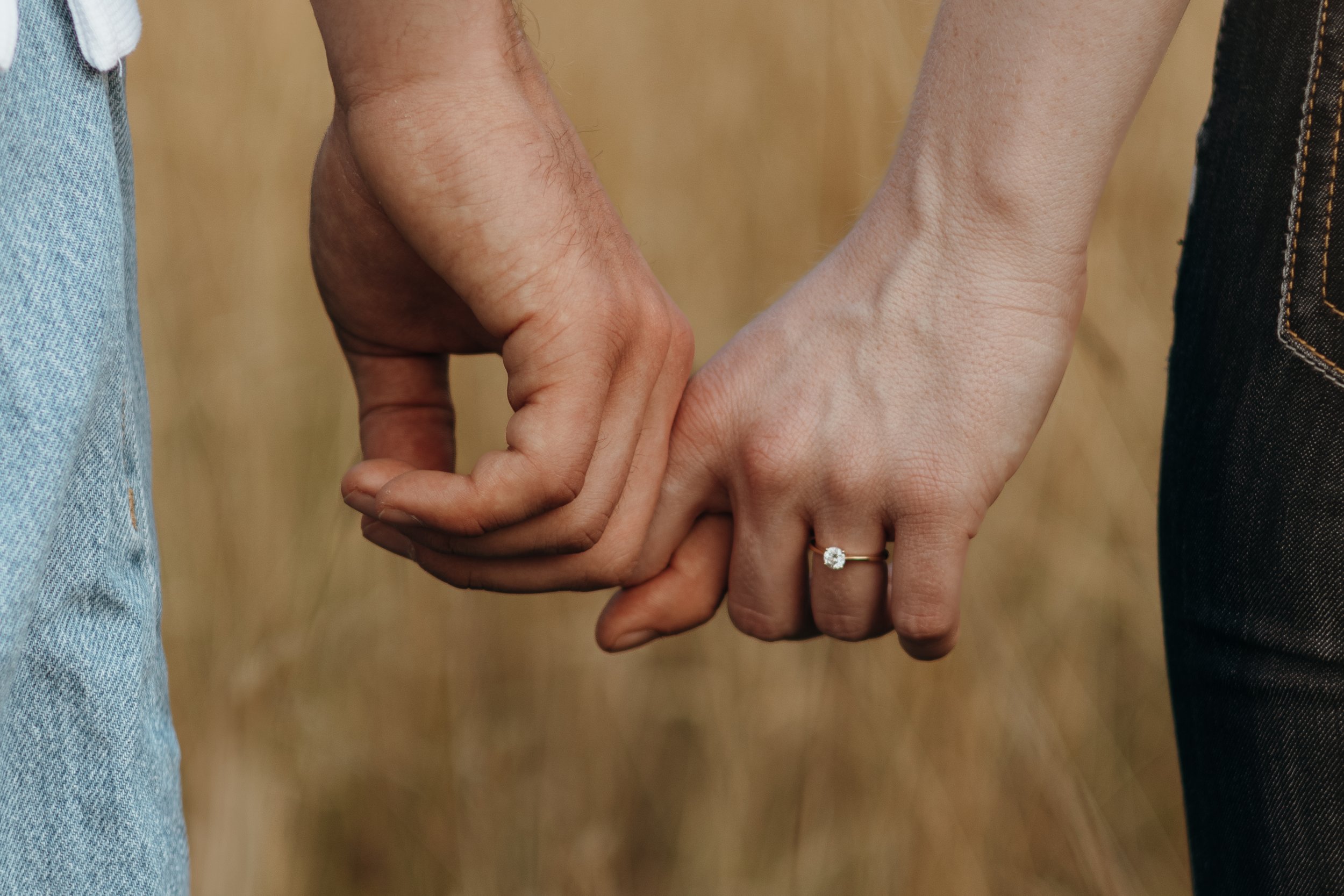 Zwei Menschen halten sich an den Händen, eine trägt einen Verlobungsring mit Diamant.