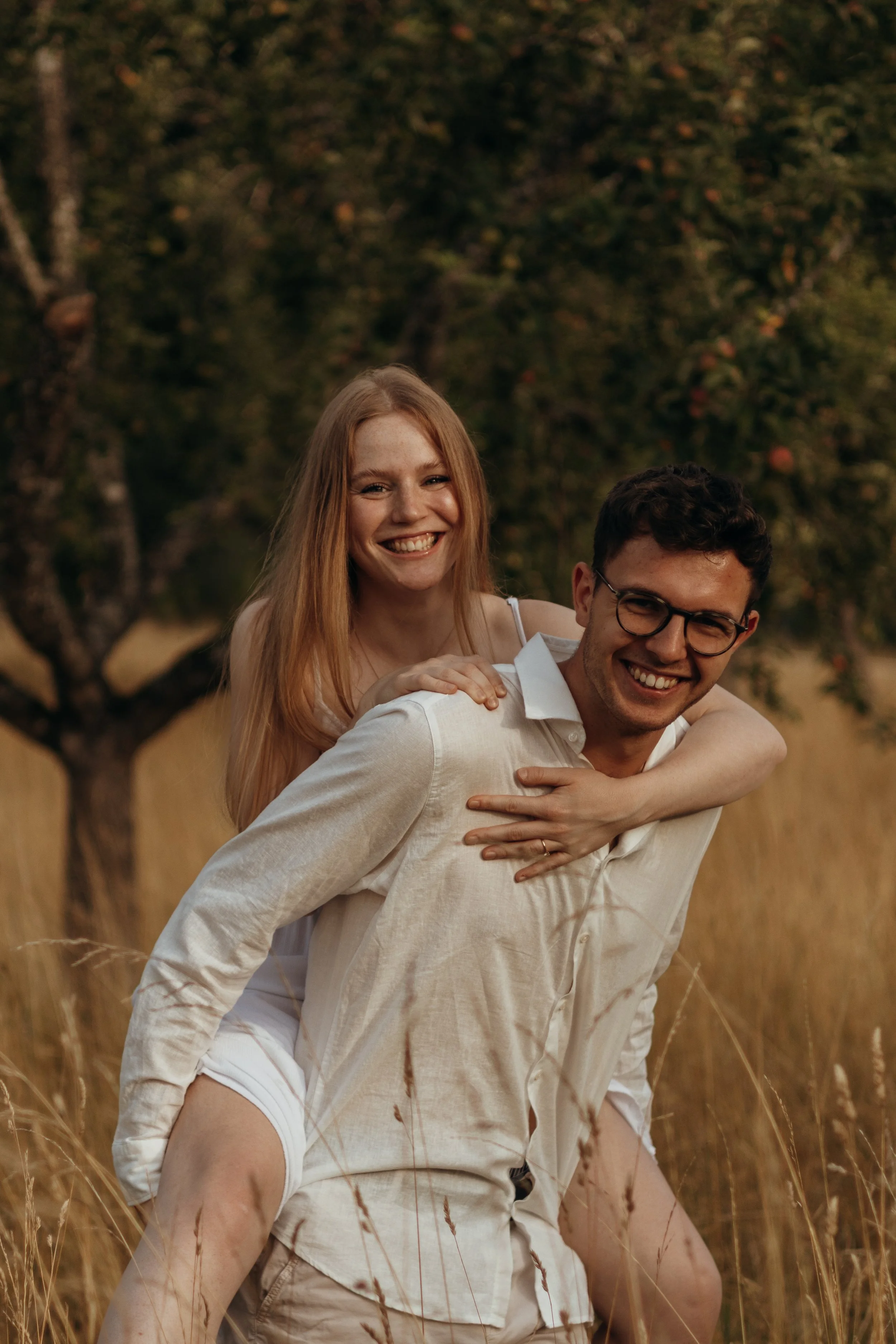 Ein glückliches Paar im Sommer auf einer Wiese, die Frau klebt auf dem Rücken des Mannes, beide lachen und genießen die Natur.