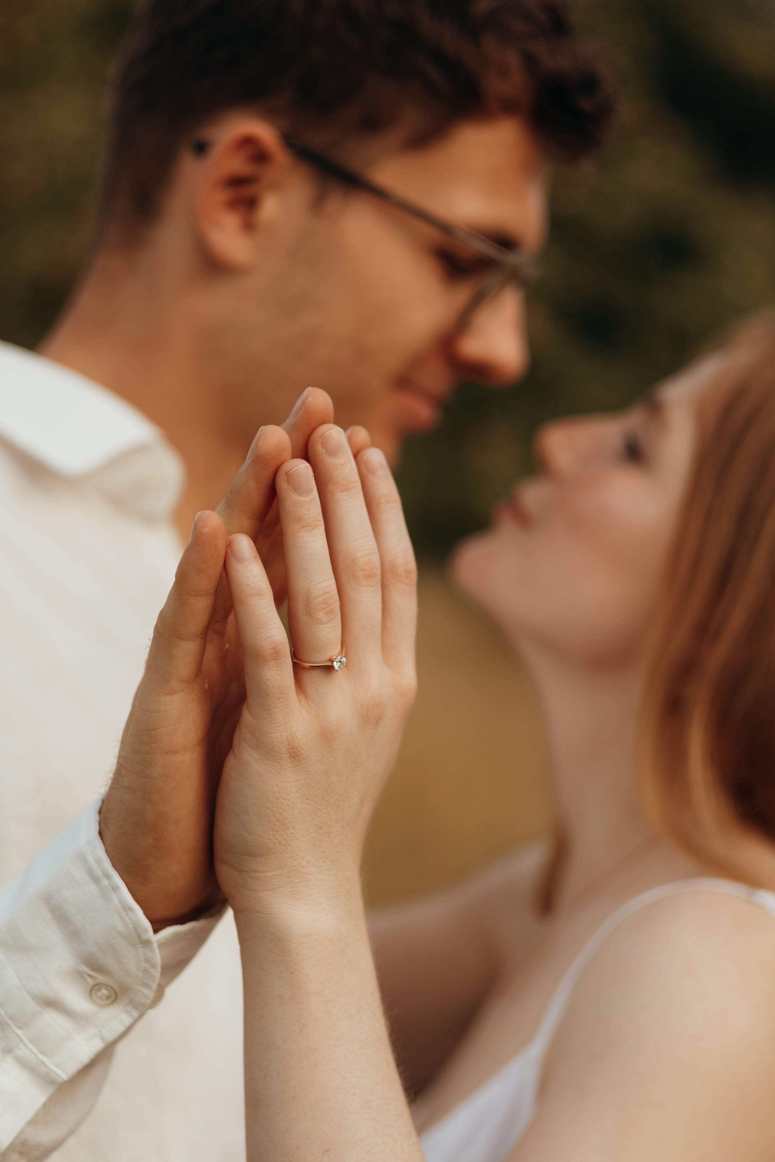 Paar streichelt sich liebevoll, Fokus auf die Hand mit Verlobungsring, verschwommene Gesichter im Hintergrund.