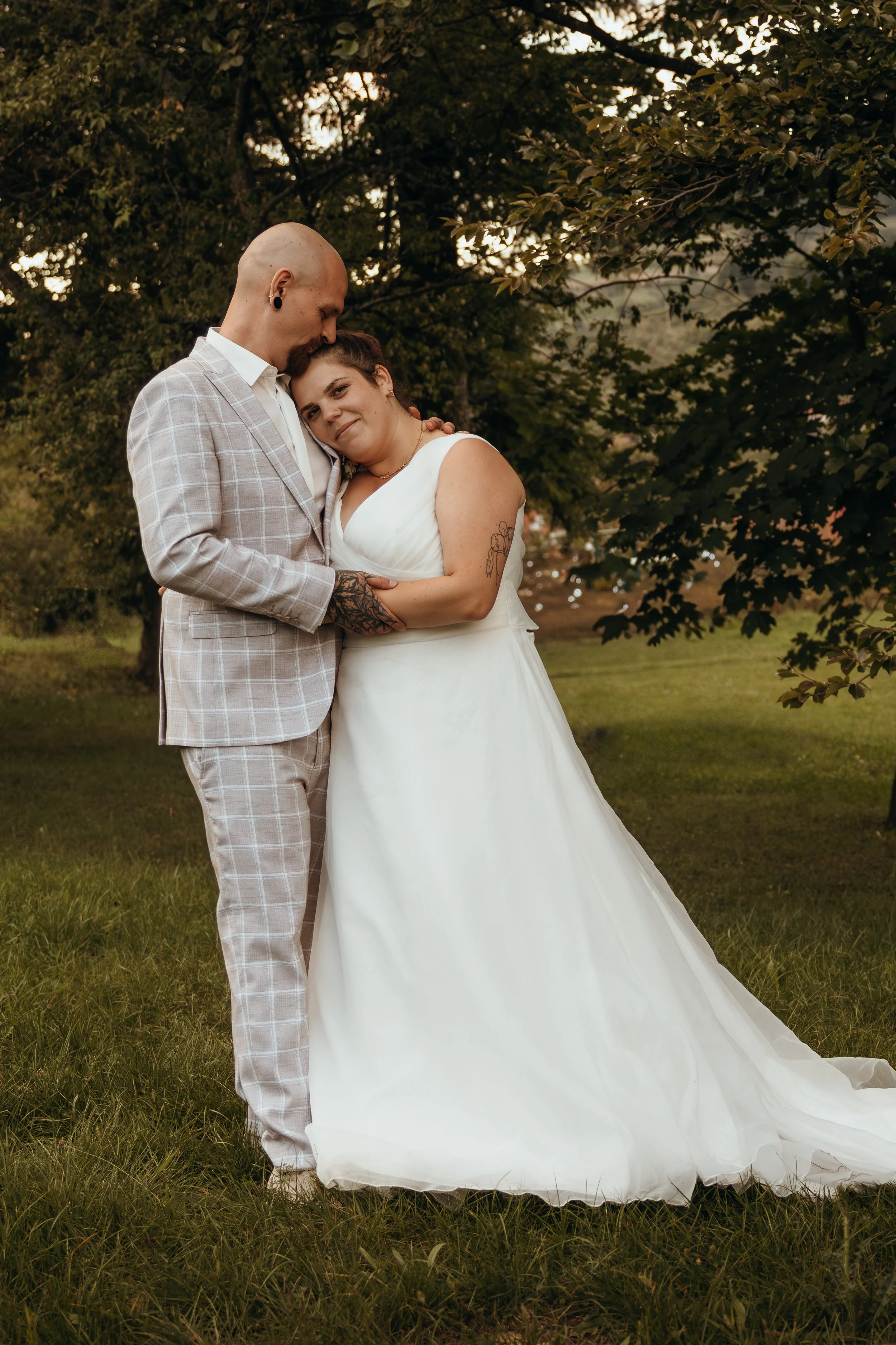 Ein Paar in Hochzeitskleidung, das umarmt und liebevoll schaut, im Freien mit Bäumen bei Sonnenuntergang.