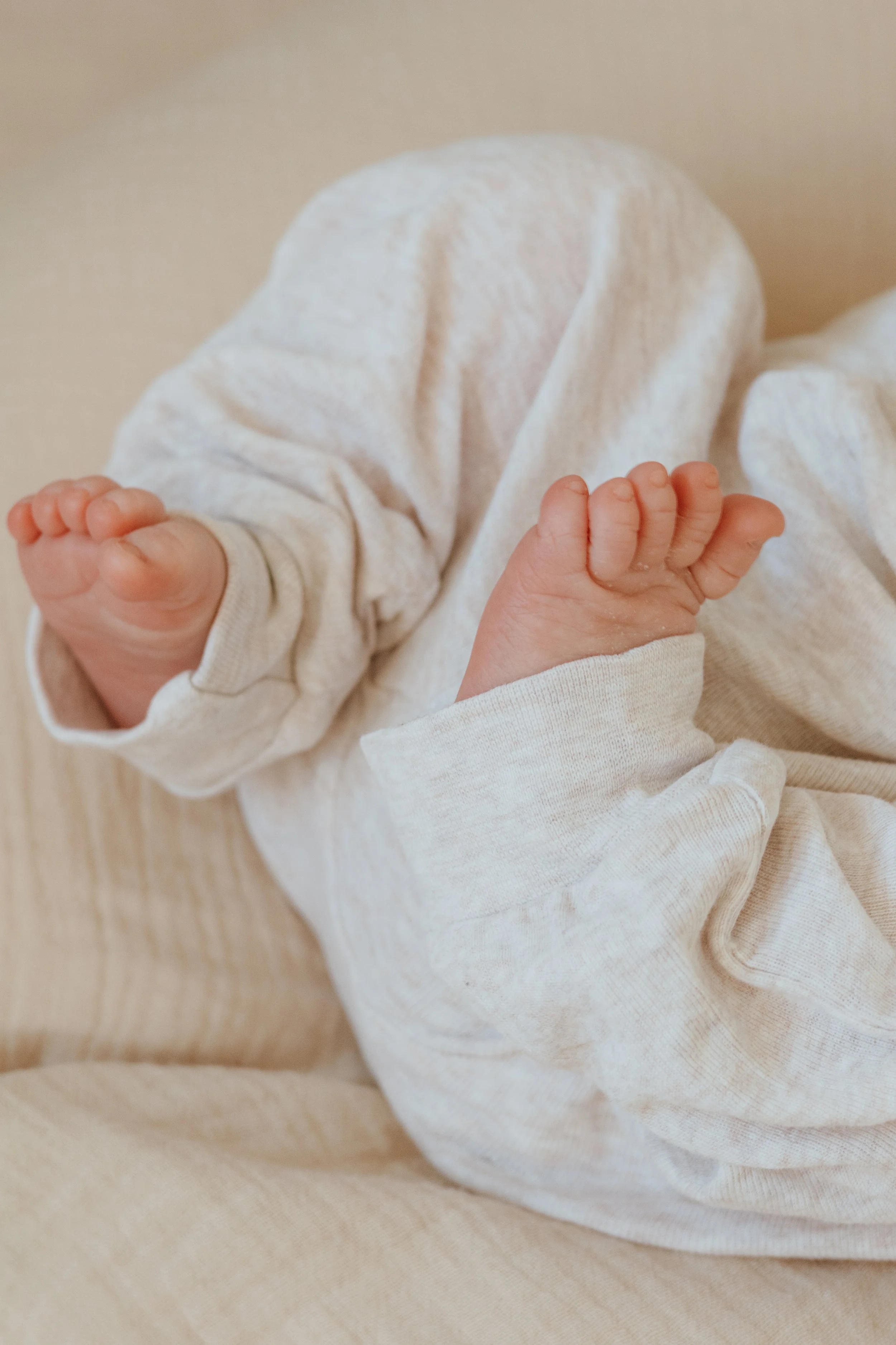 Nahaufnahme von Babyfüßen, die in einer weißen, langärmligen Kleidung ruhen.