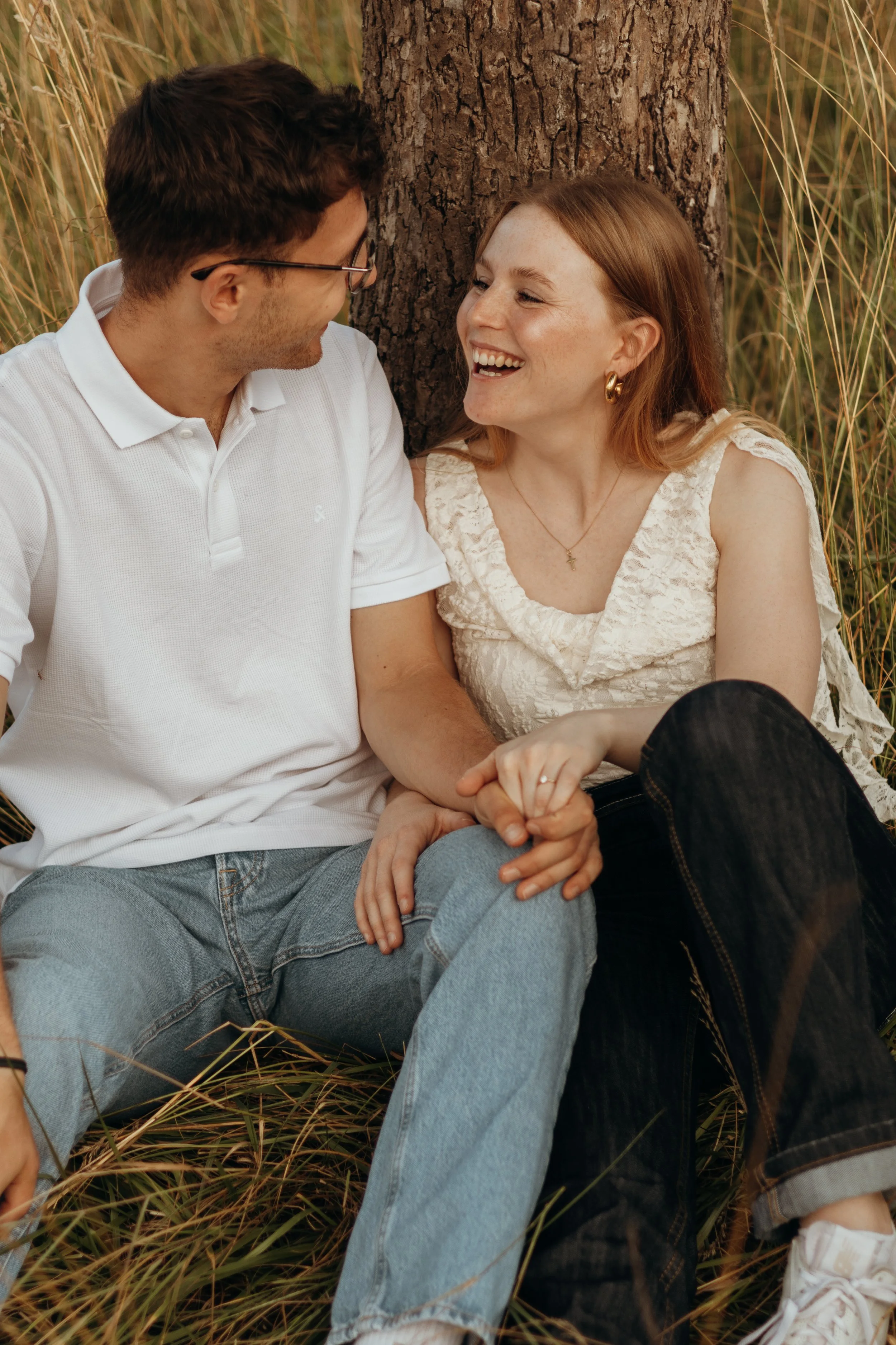 Ein lachendes Paar sitzt an einem Baum in einem Graselement im Freien.