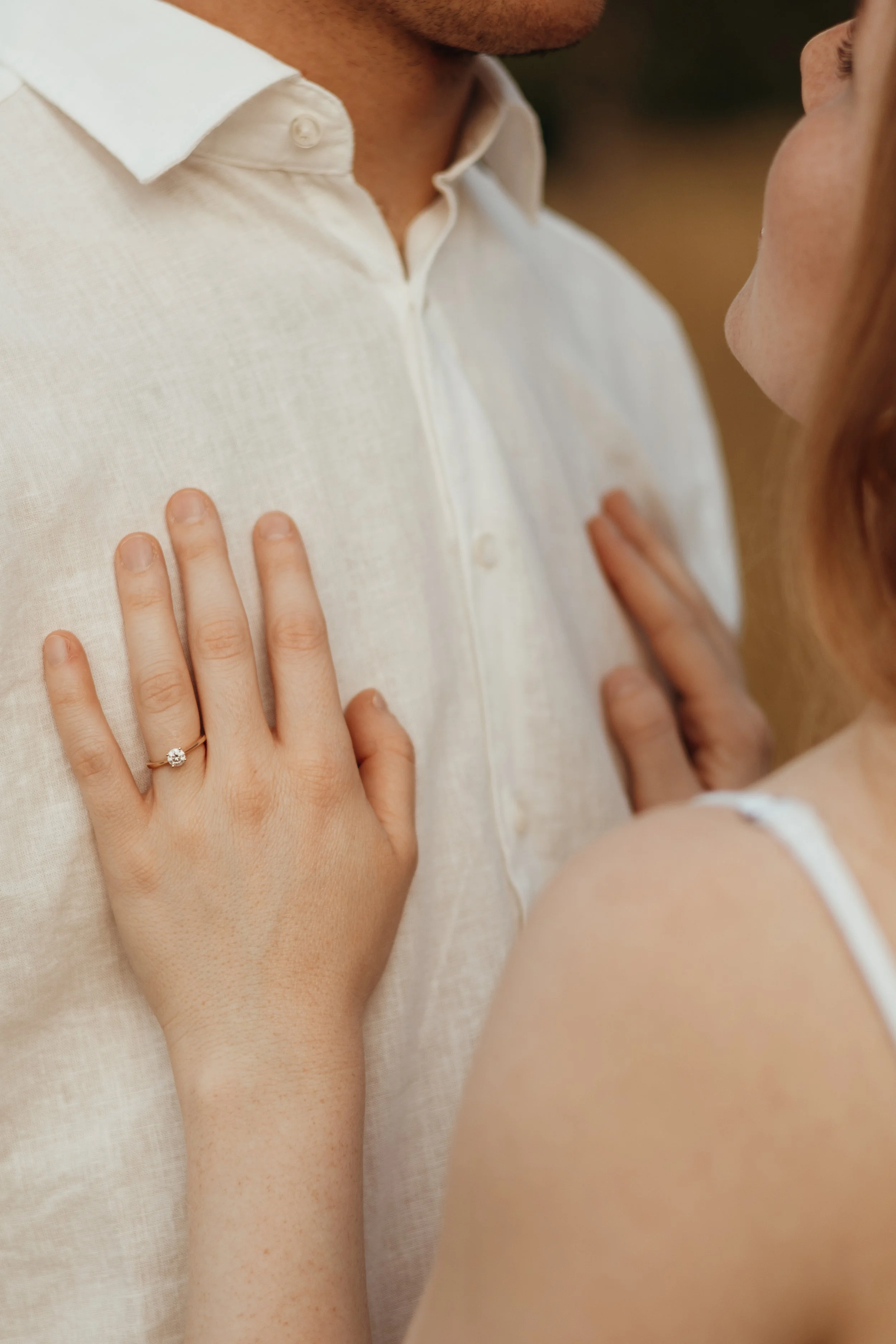 Nahaufnahme eines Paares, bei dem die Frau ihre Hand mit einem Verlobungsring auf die Brust des Mannes legt.